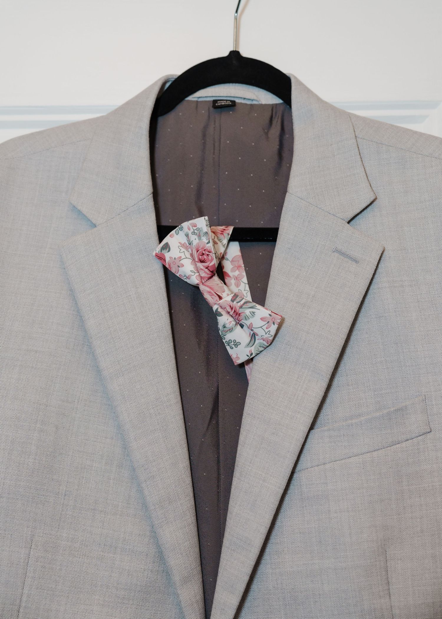 Light grey suit jacket hangs with floral bow tie displayed on hanger.
