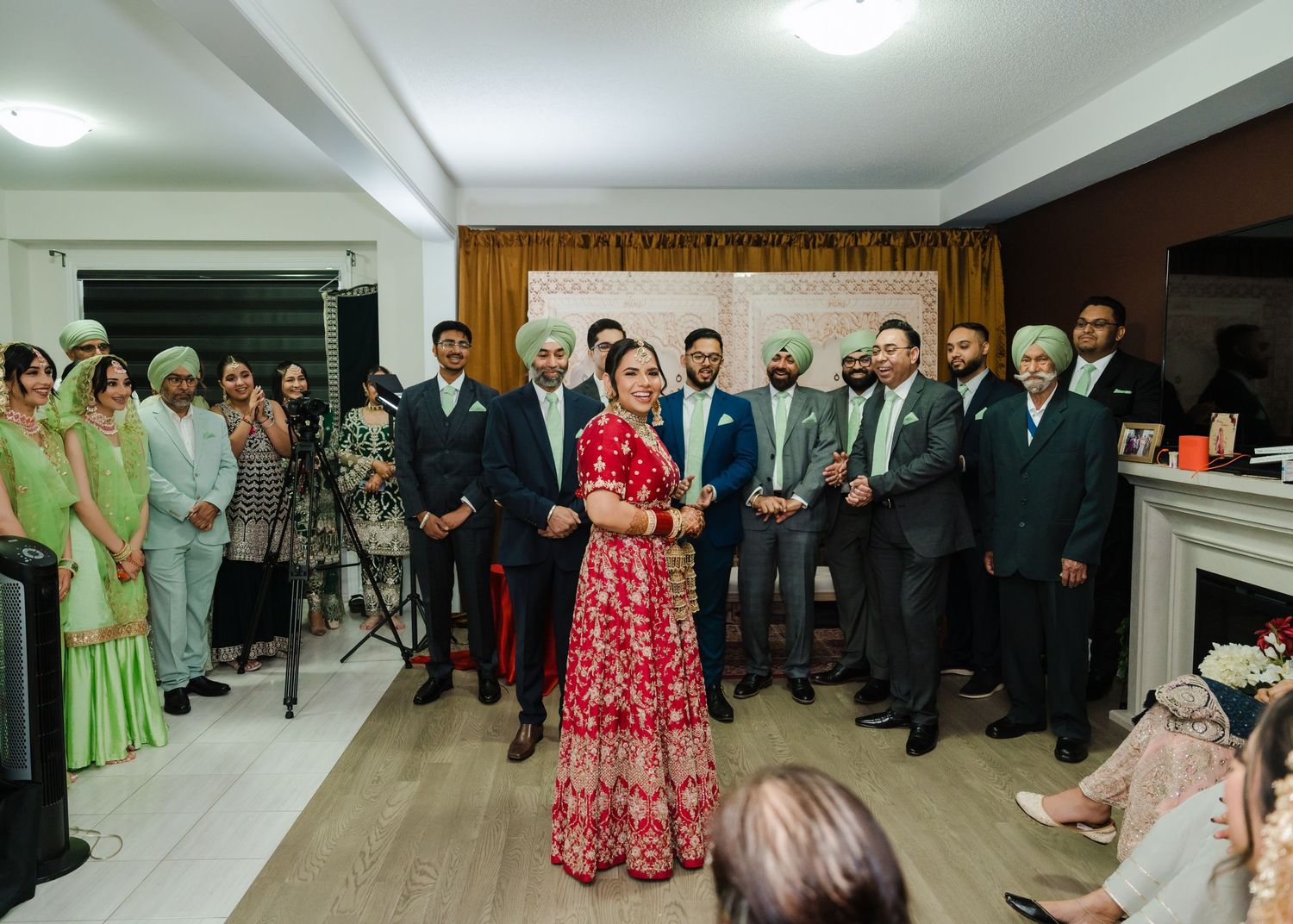 A wedding celebration showing the bride in a traditional red lehenga surrounded by guests at an indoor venue.