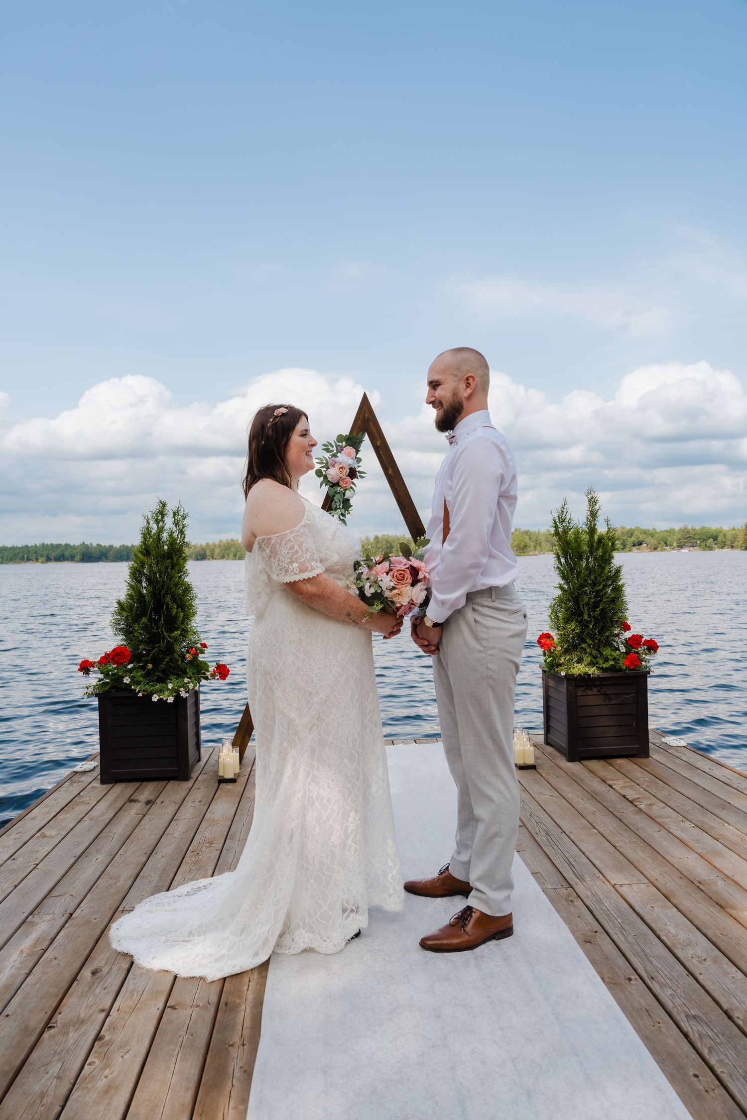 Couple exchanges vows during intimate lakeside dock wedding ceremony with flowers and white aisle runner.