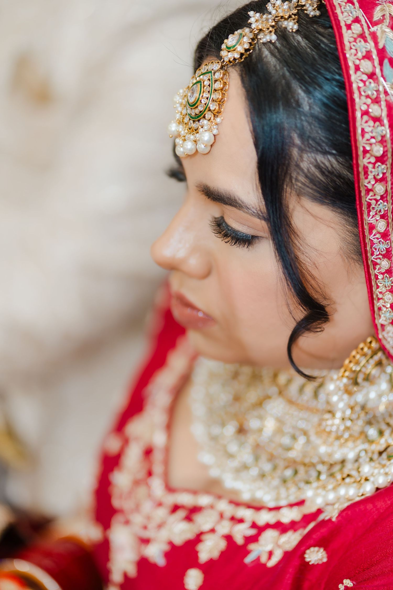 Close up profile view of traditional Indian bridal jewelry and makeup details with red and gold attire.