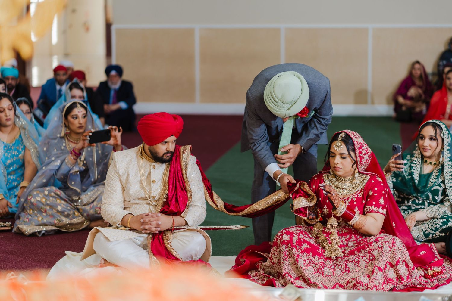 People seated on the floor during a traditional Sikh wedding ceremony with the couple in traditional red attire.