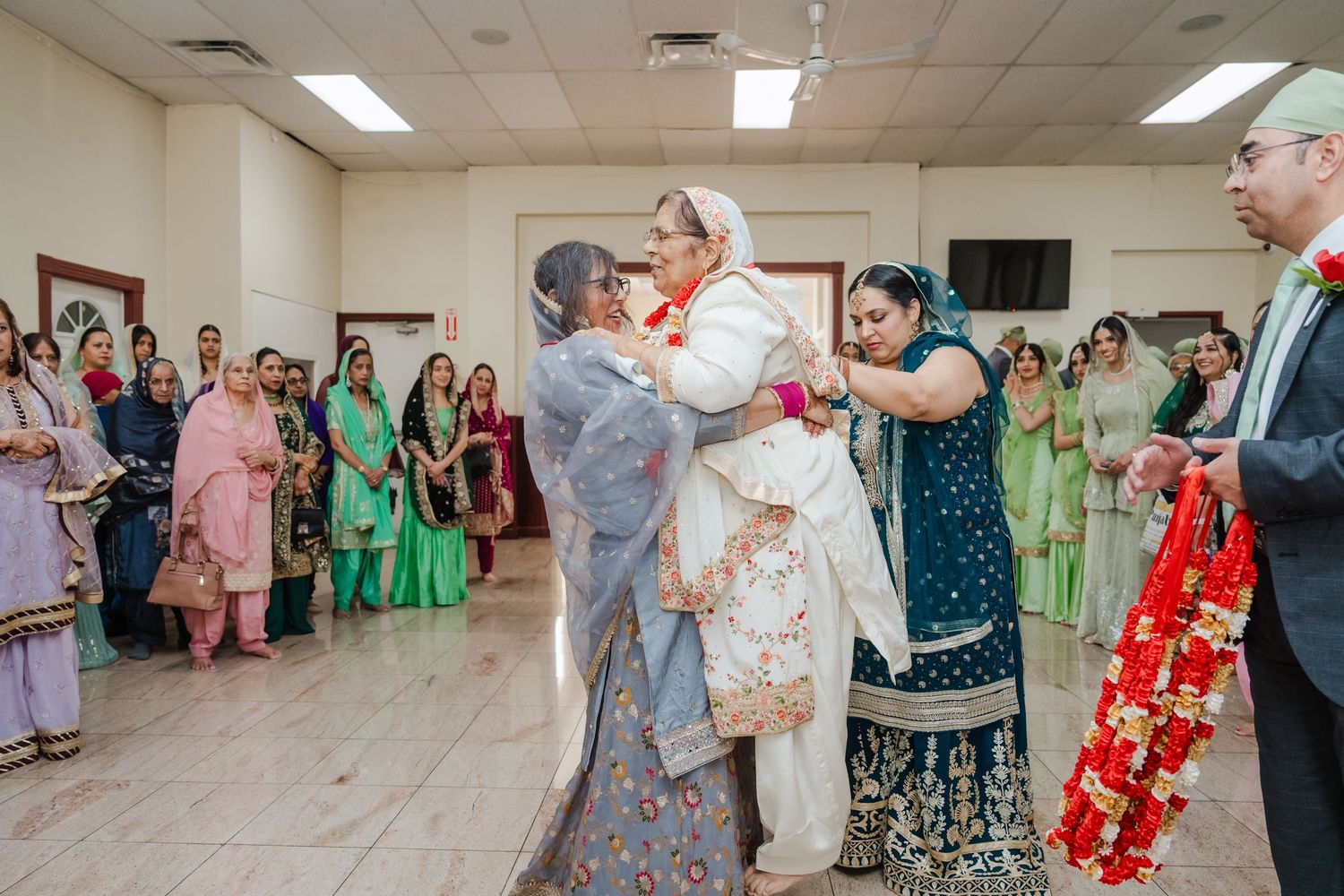 Wedding guests in colorful traditional attire gather around a couple dancing at a reception celebration.