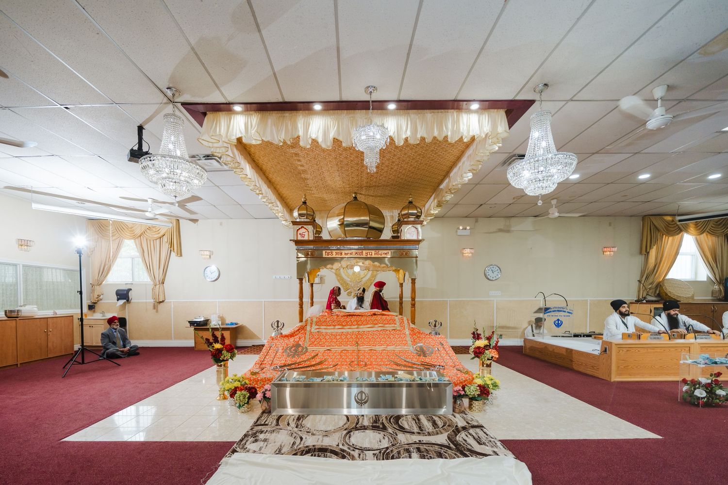An ornate religious ceremony space with chandeliers, orange fabric draping, and red carpeting in a banquet hall.