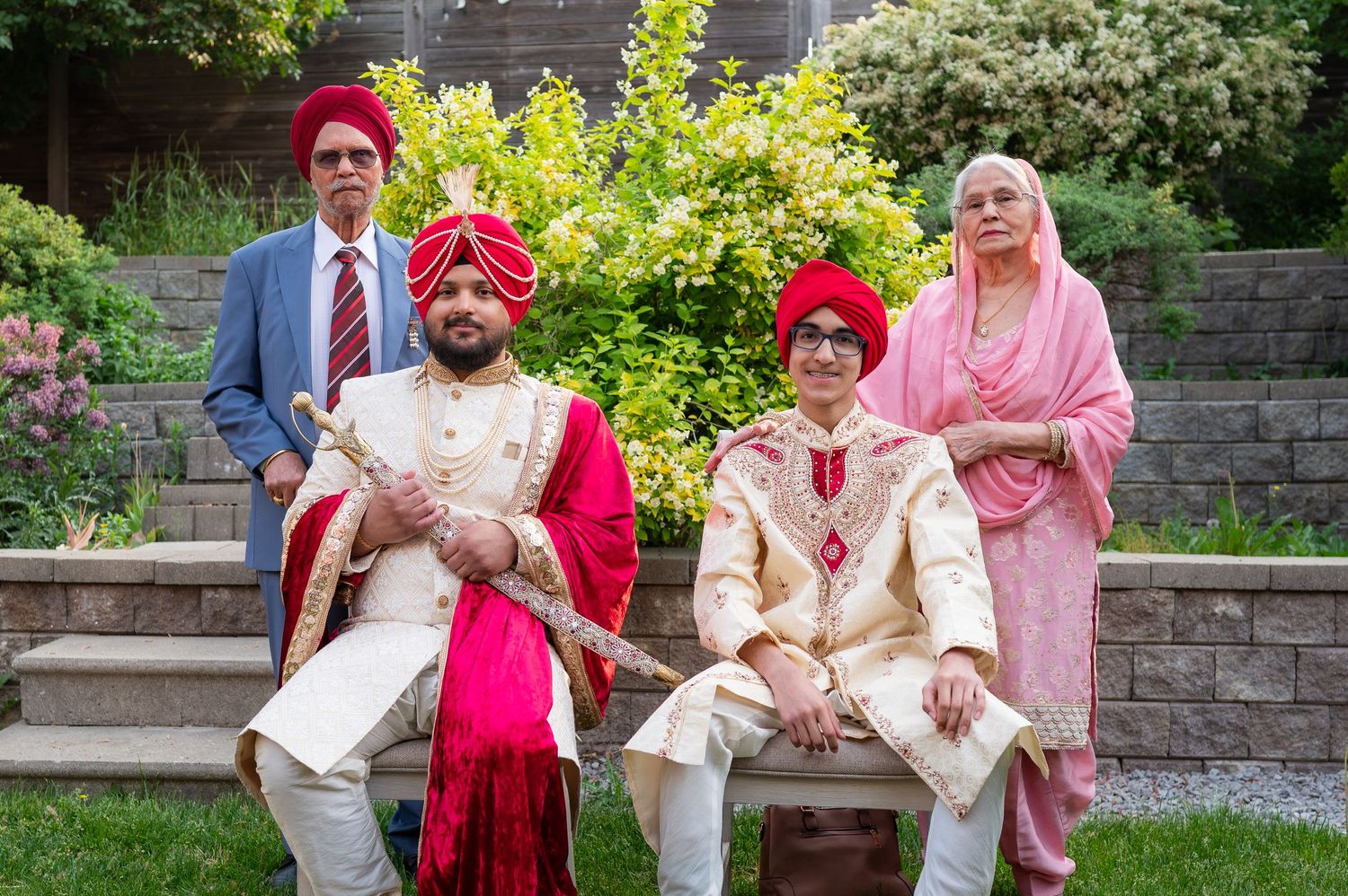 Family group in traditional Sikh wedding attire seated on stone steps in a garden.
