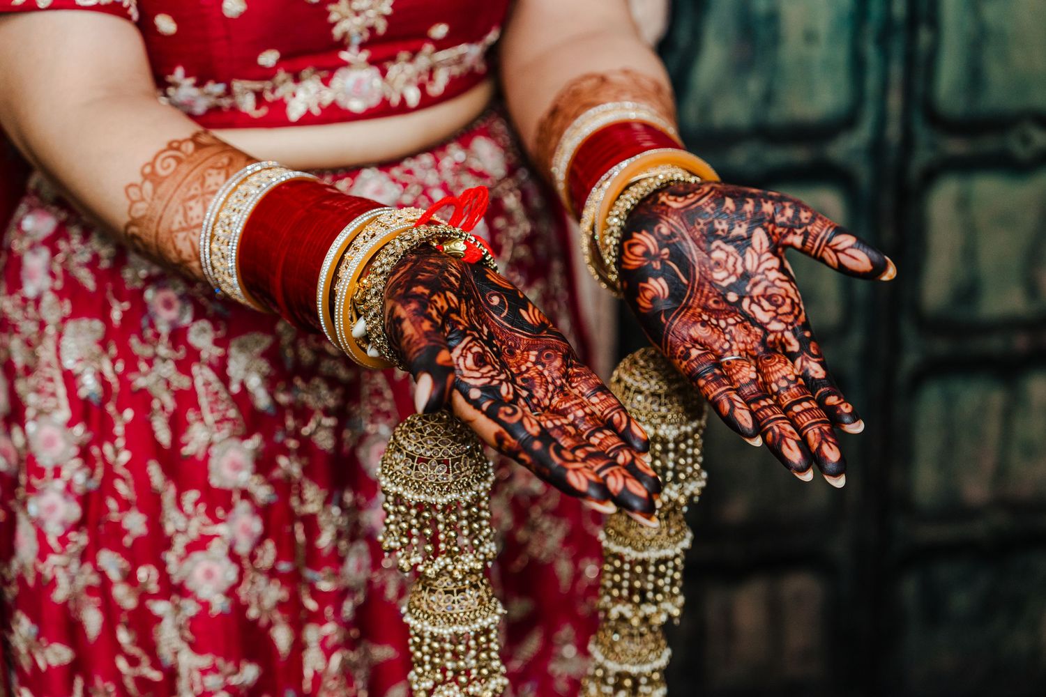 Detailed henna designs adorn hands decorated with gold bangles and traditional Indian bridal jewelry.