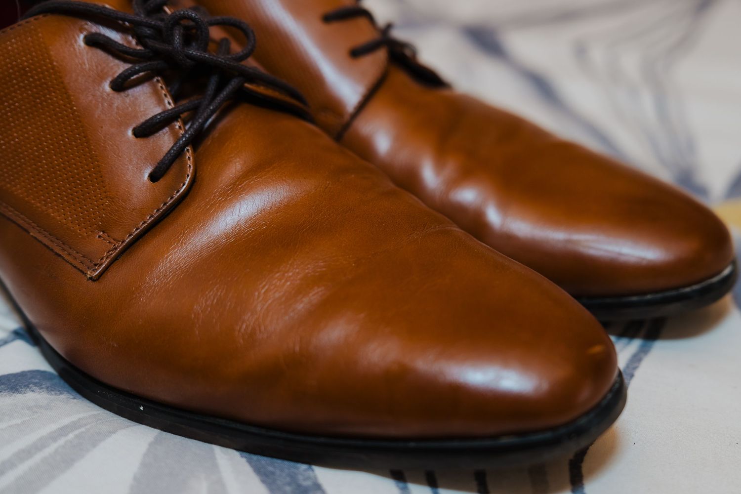 A pair of polished tan leather Oxford dress shoes with black laces against a light background.