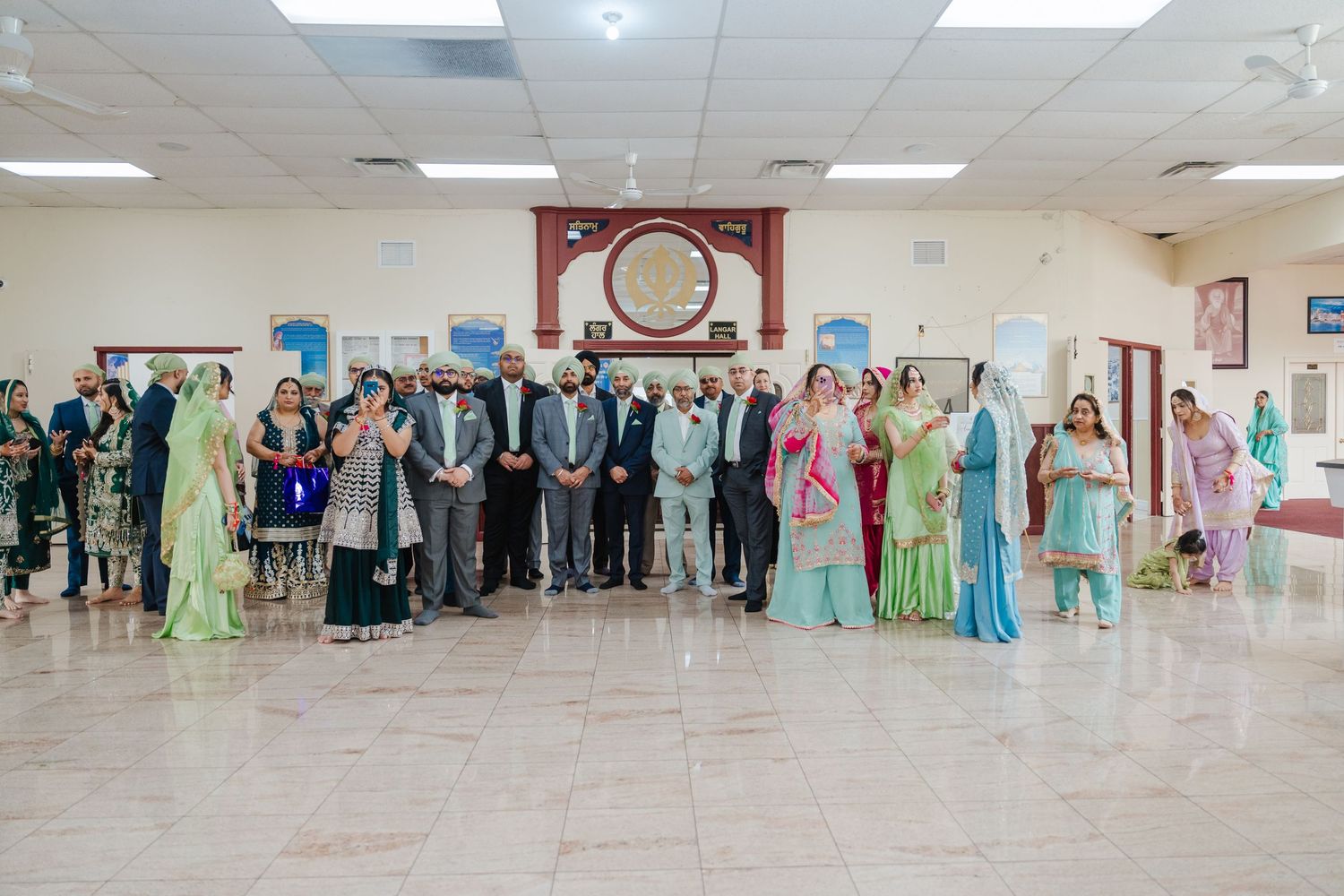 A wedding celebration showing guests of various nationalities gathered in a bright reception hall wearing cultural and formal attire.