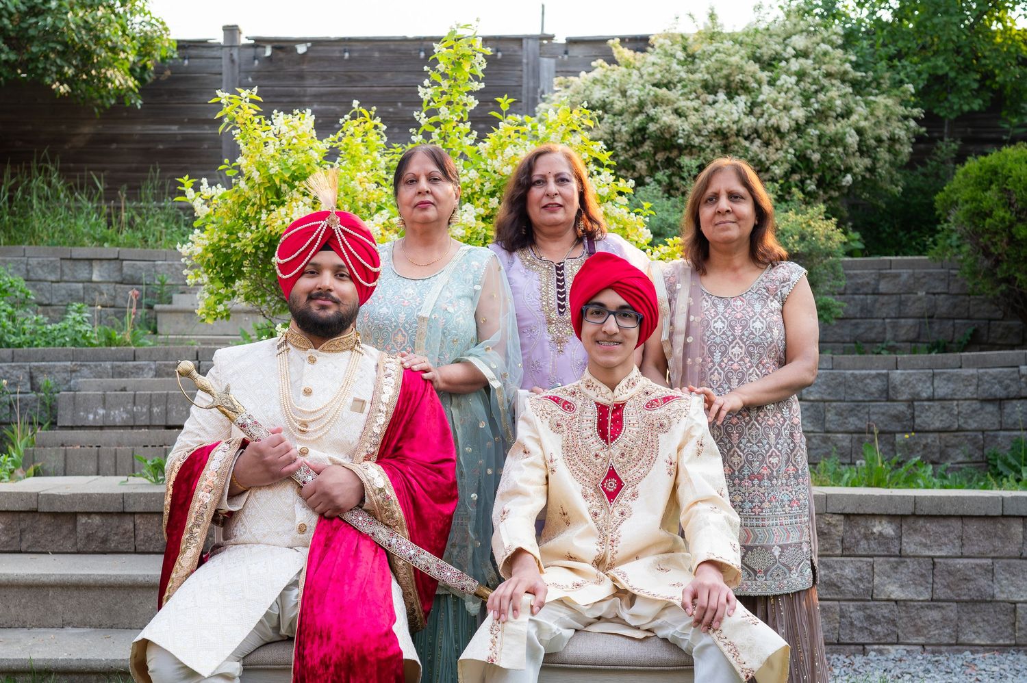 Group photo of wedding party members in traditional Sikh and Western attire on outdoor stone steps.