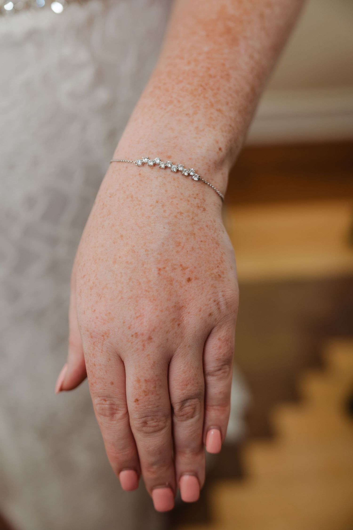 Delicate silver bracelet adorns wrist against lace fabric background.