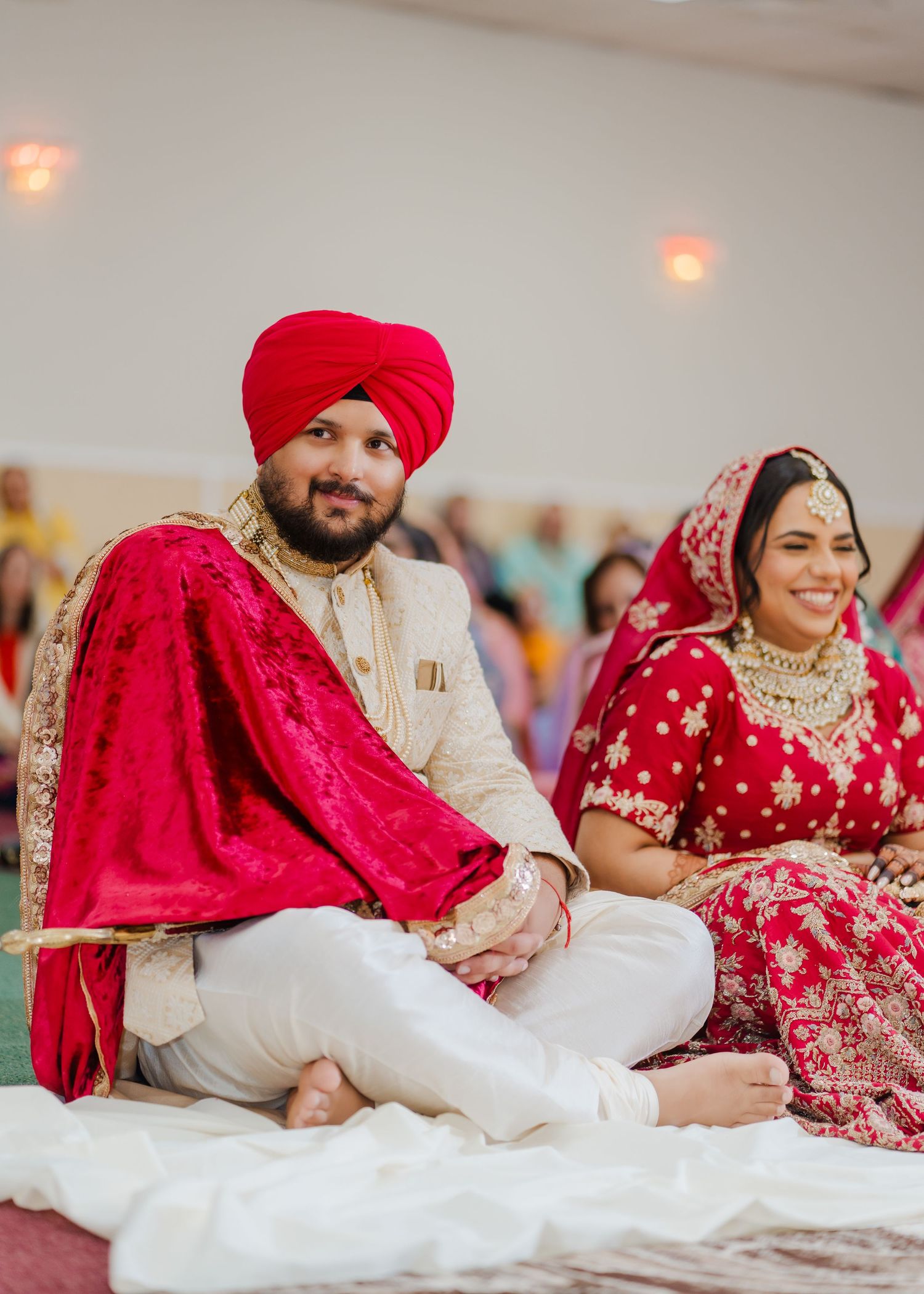 Traditional Sikh couple in red and white attire seated during wedding ceremony.