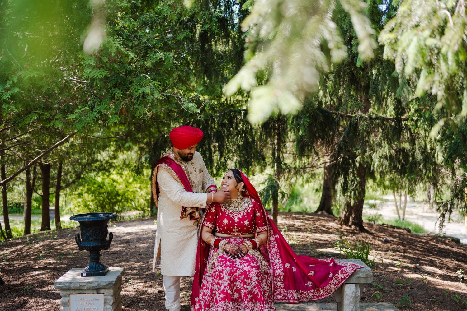 Wedding couple in traditional Sikh attire performing ceremony under evergreen trees.