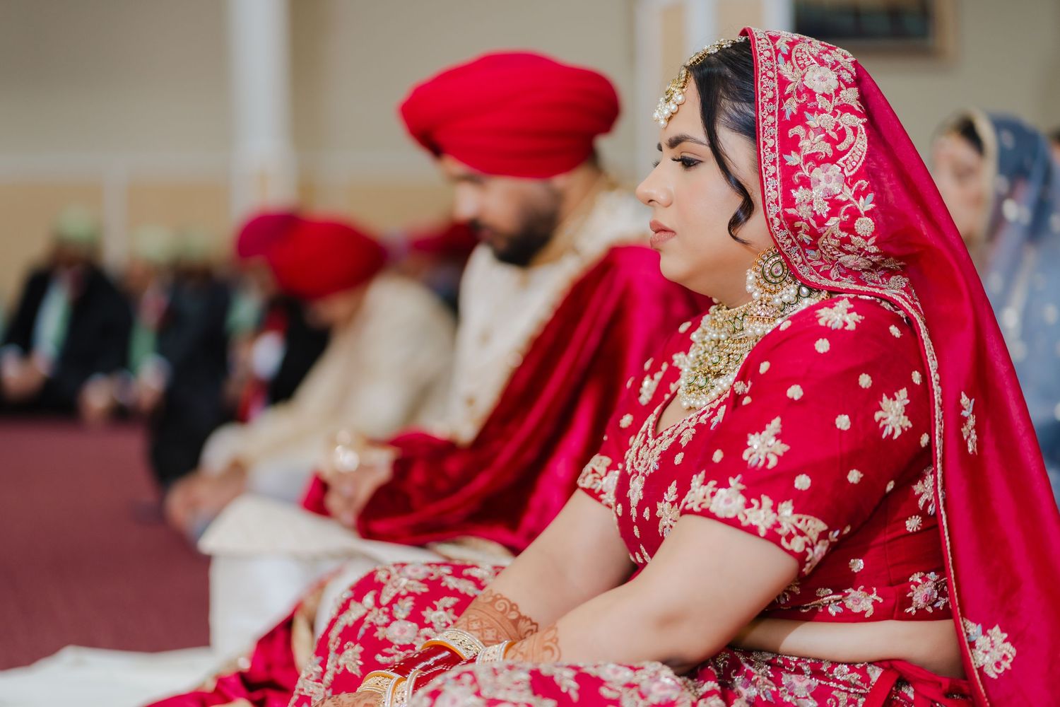 Traditional Sikh wedding ceremony with couple in ornate red attire seated during religious proceedings.