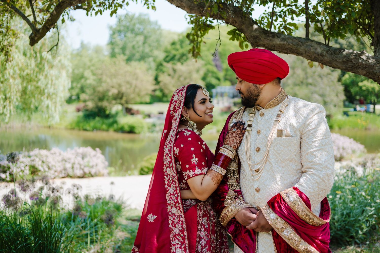 Couple in traditional Sikh wedding attire posing in a lush garden setting.