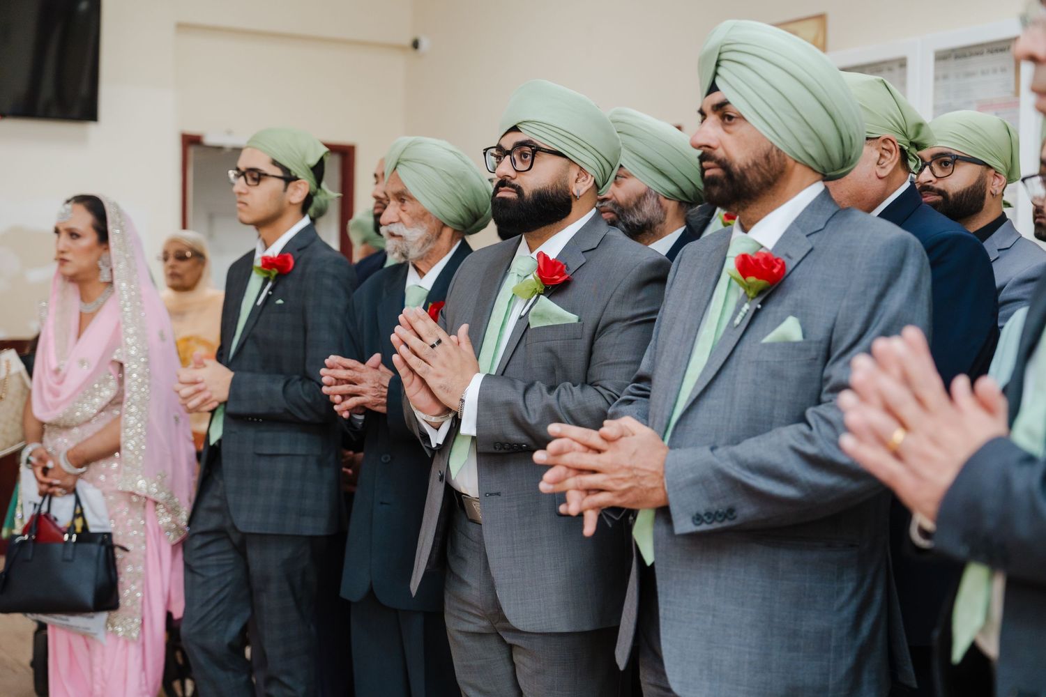 Groomsmen wearing matching mint green turbans and gray suits standing in a row during Sikh wedding ceremony.