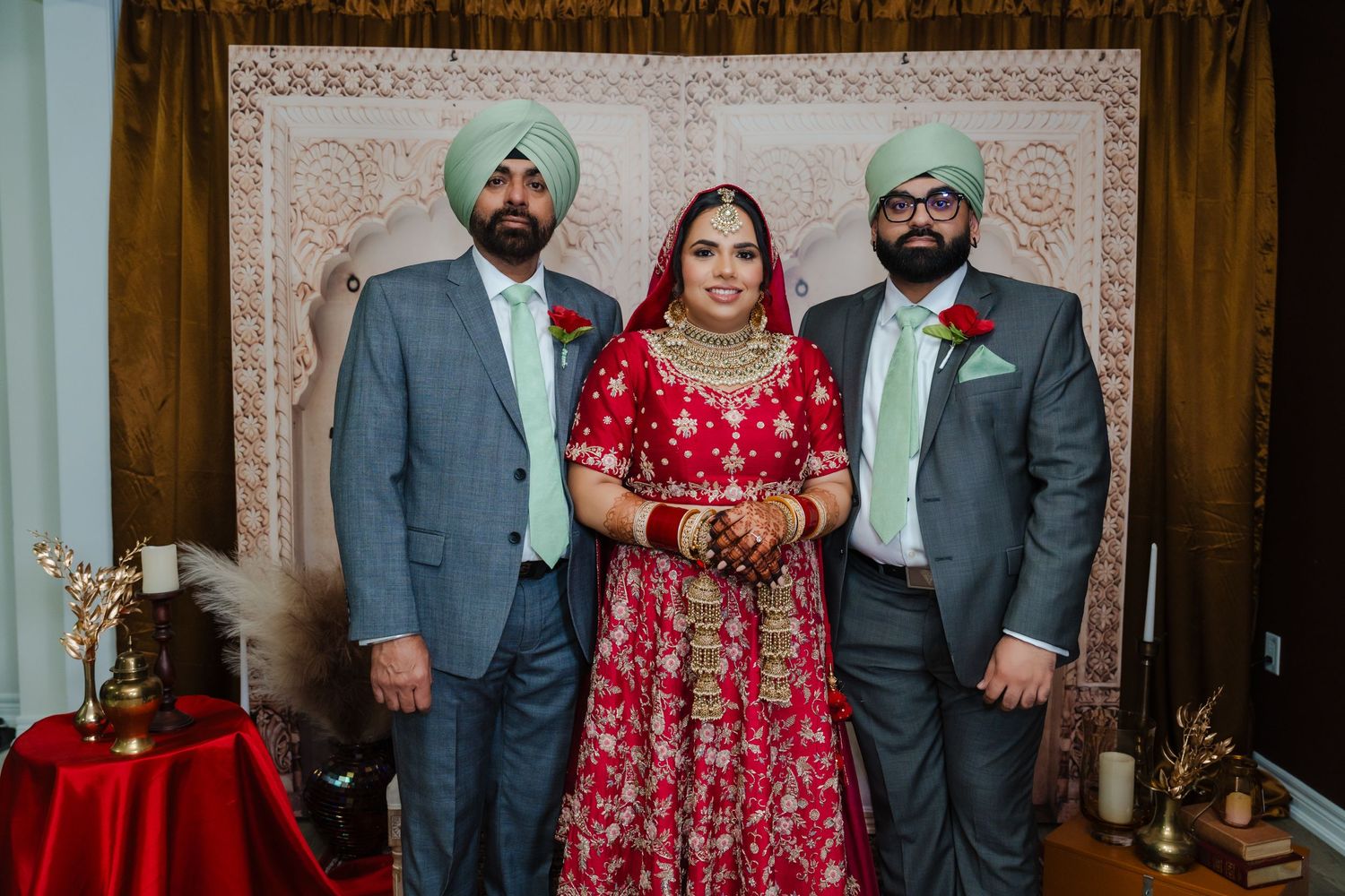 Formal portrait of bride in red traditional dress with two attendants in grey suits.