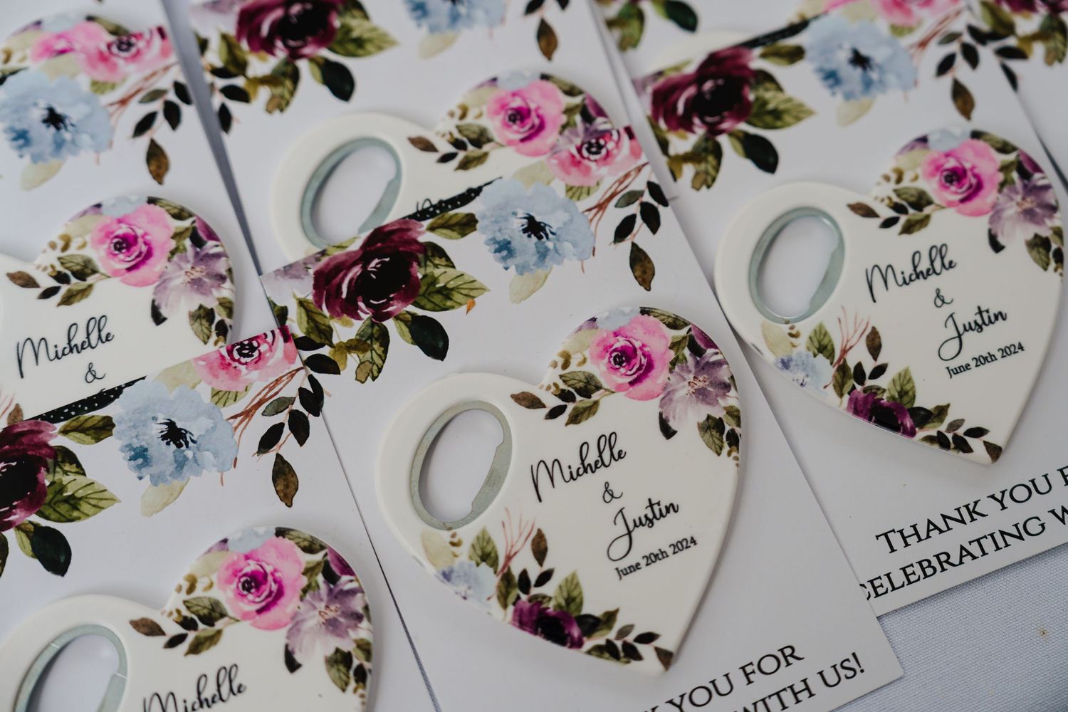 Wedding favor tags with pink and blue floral designs and silver rings decorating white heart-shaped cards.
