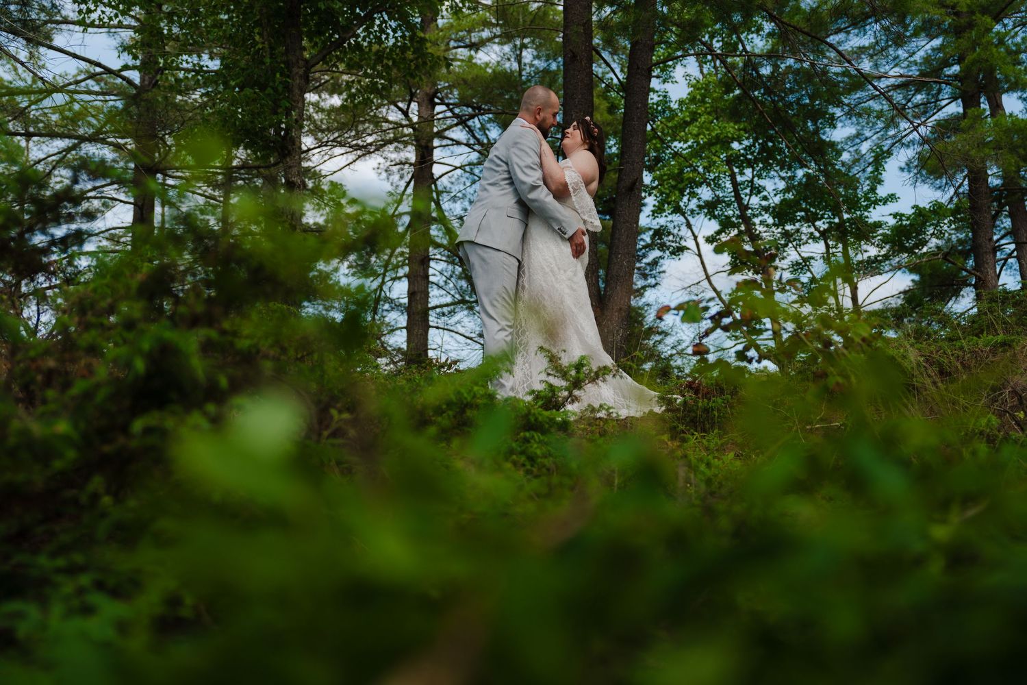 A couple embraces on a hilltop surrounded by evergreen trees in soft focus.