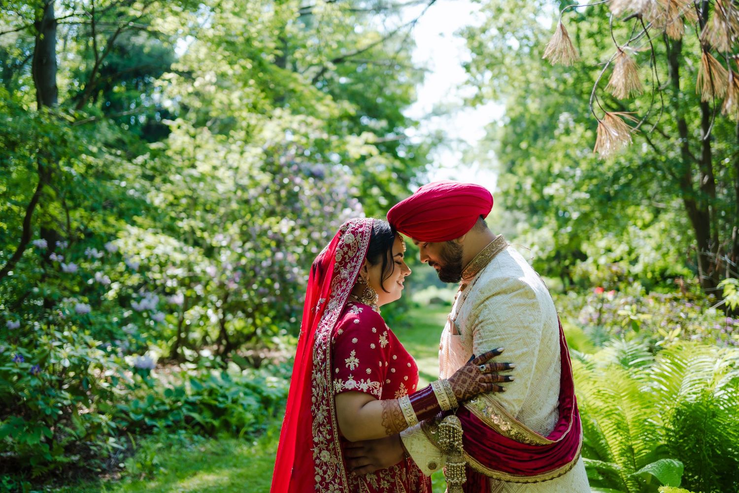 A couple in traditional Indian wedding attire share an intimate moment in a lush garden setting.