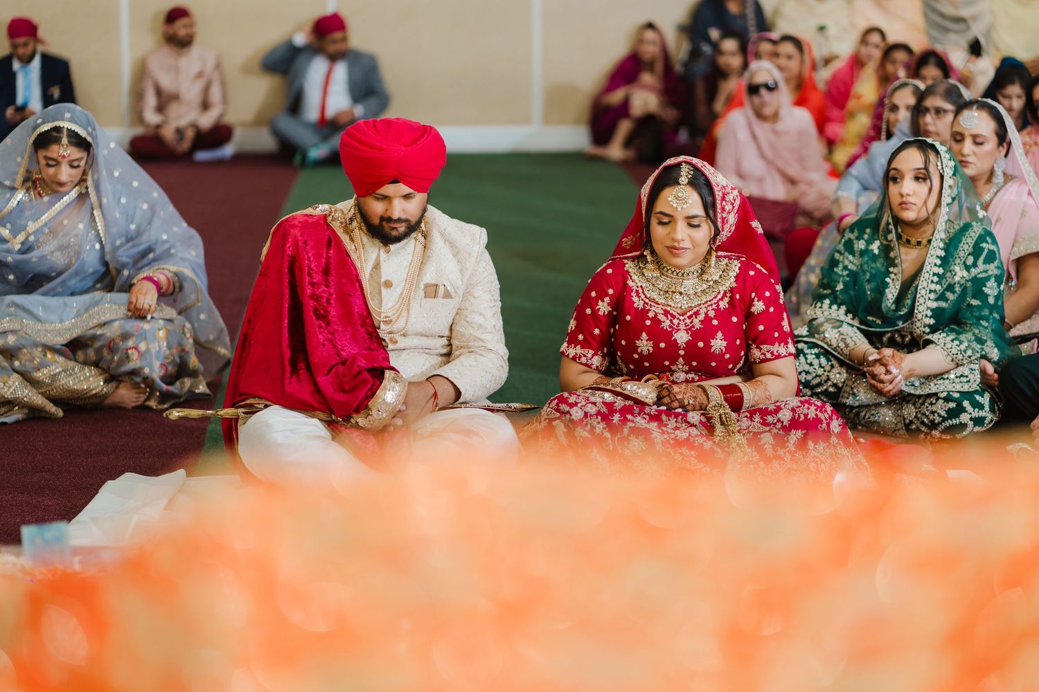 Traditional Sikh ceremony attendees seated on floor during religious gathering wearing colorful traditional attire.
