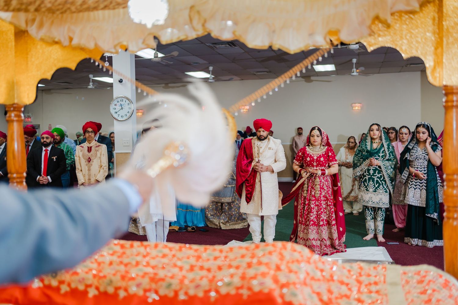 Celebratory moment at Sikh wedding ceremony with guests and decorative elements in background.