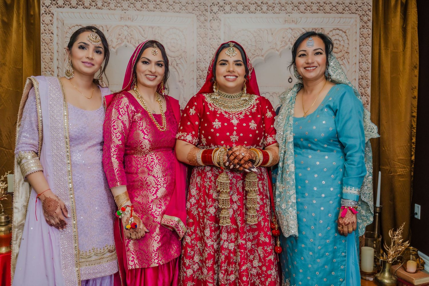 Four women in colorful formal attire posing together at wedding celebration.
