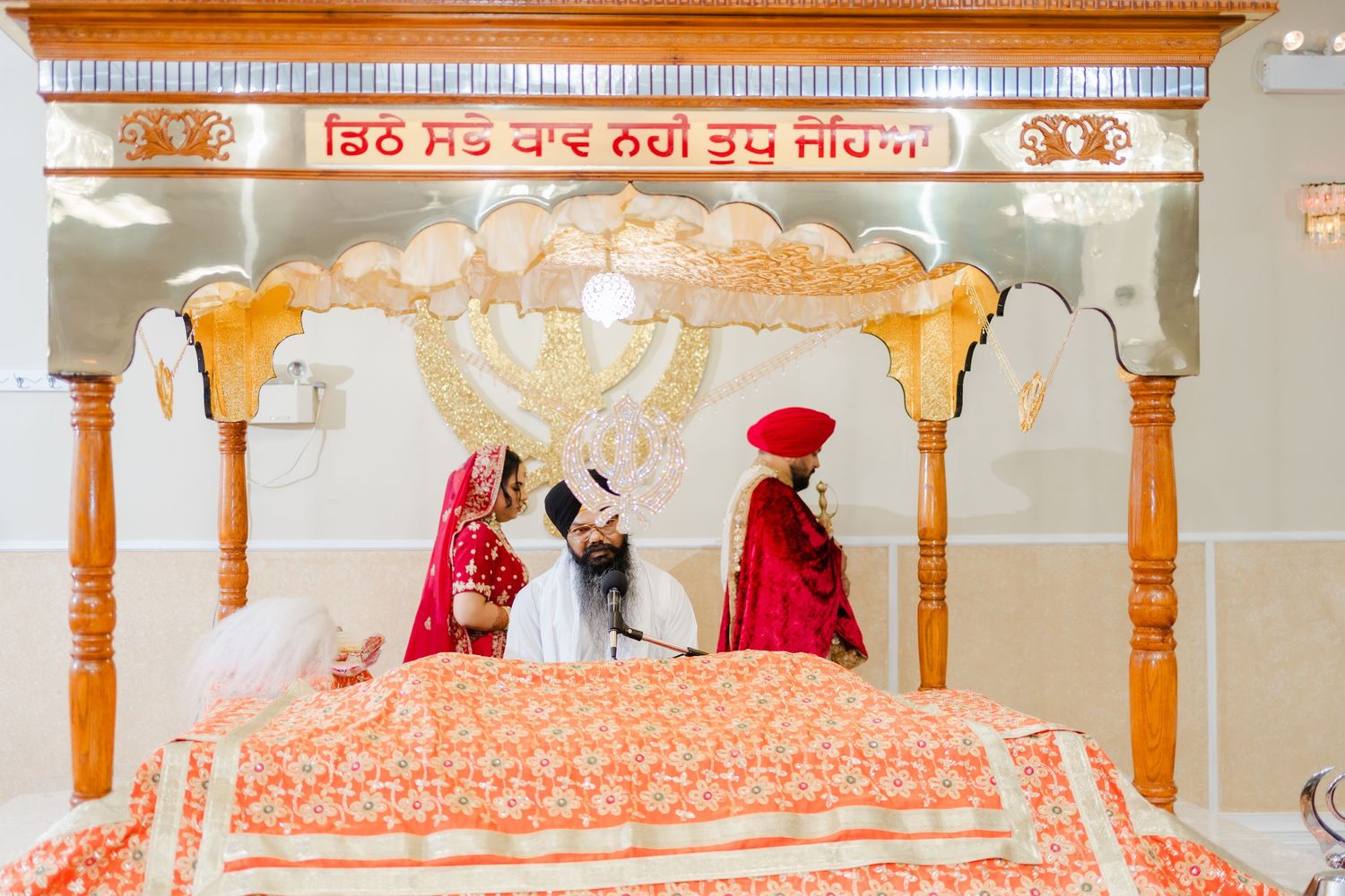 Traditional Sikh ceremony at a Gurdwara with decorative orange and gold archway over the Guru Granth Sahib.