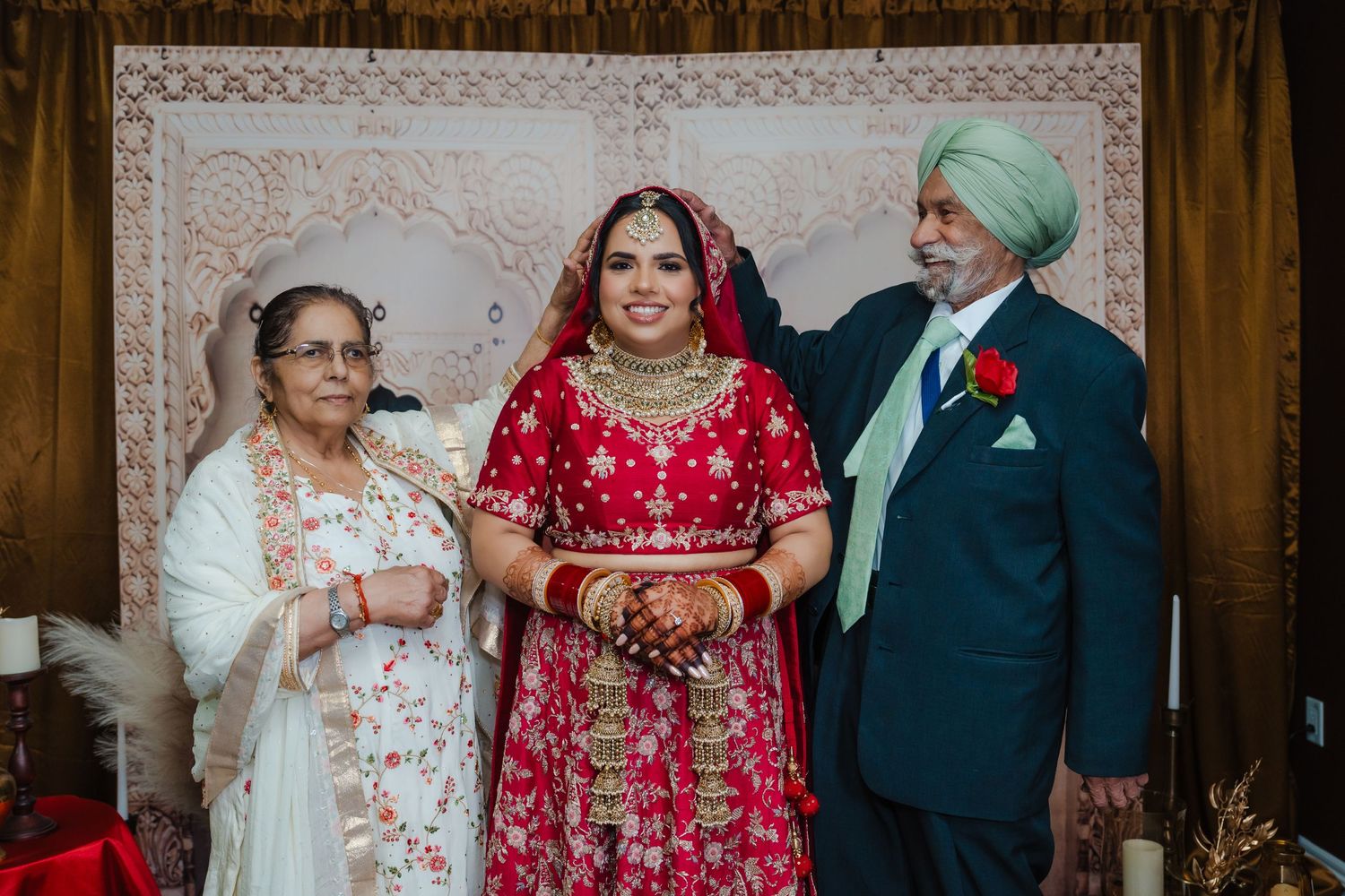 A couple in traditional Sikh wedding attire standing together with an elder family member.