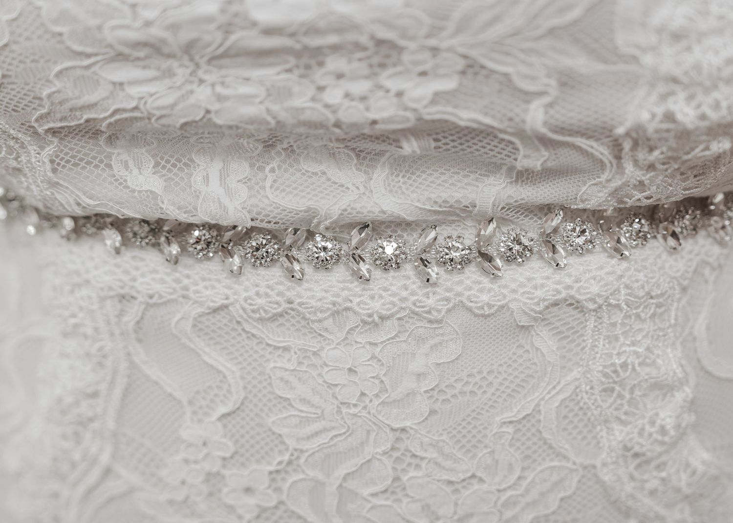 Close-up detail of delicate white lace trim and beadwork on a wedding dress.