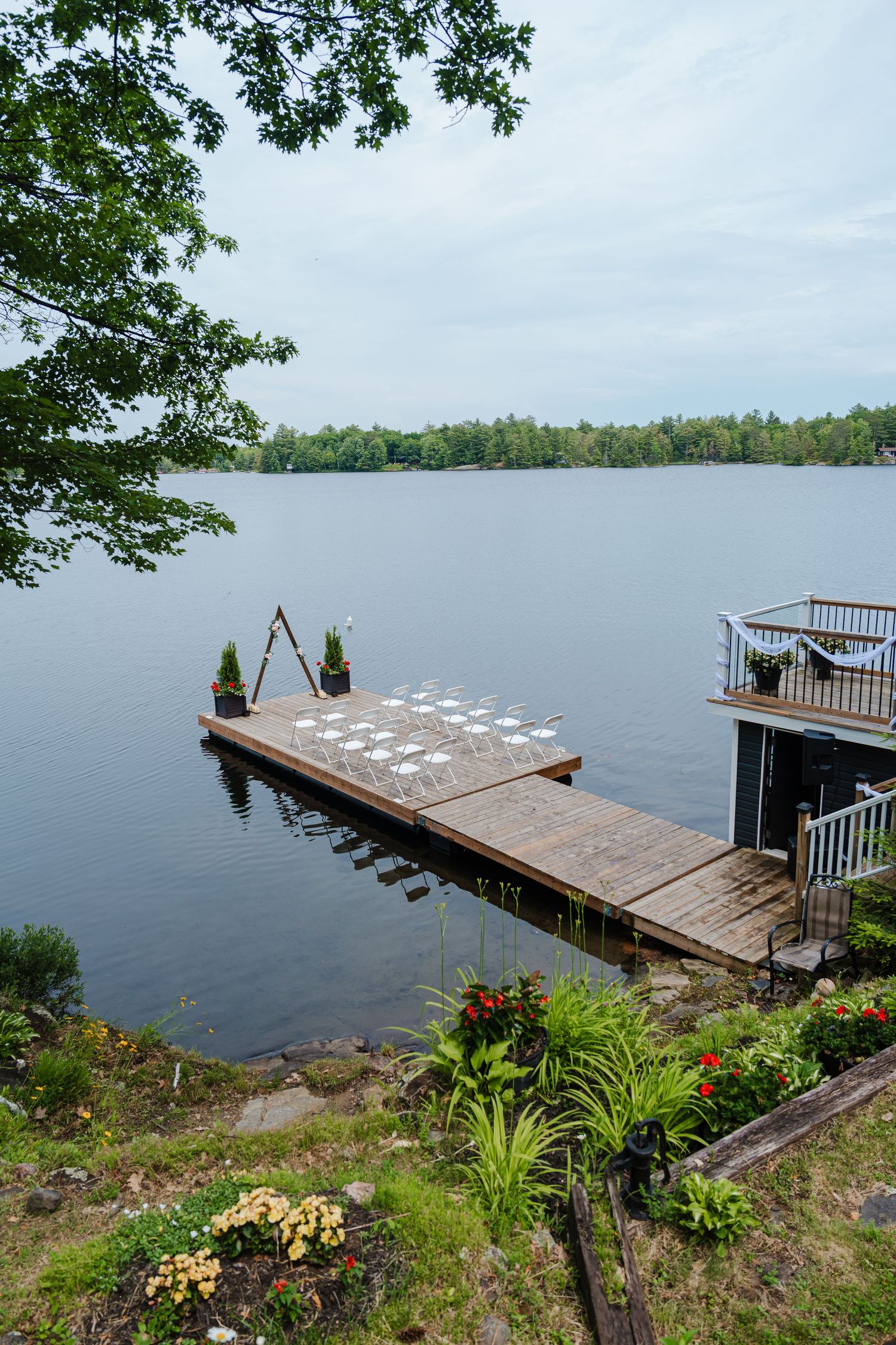 Wooden dock extends over calm lake waters with garden landscaping and trees framing the tranquil lakeside scene.