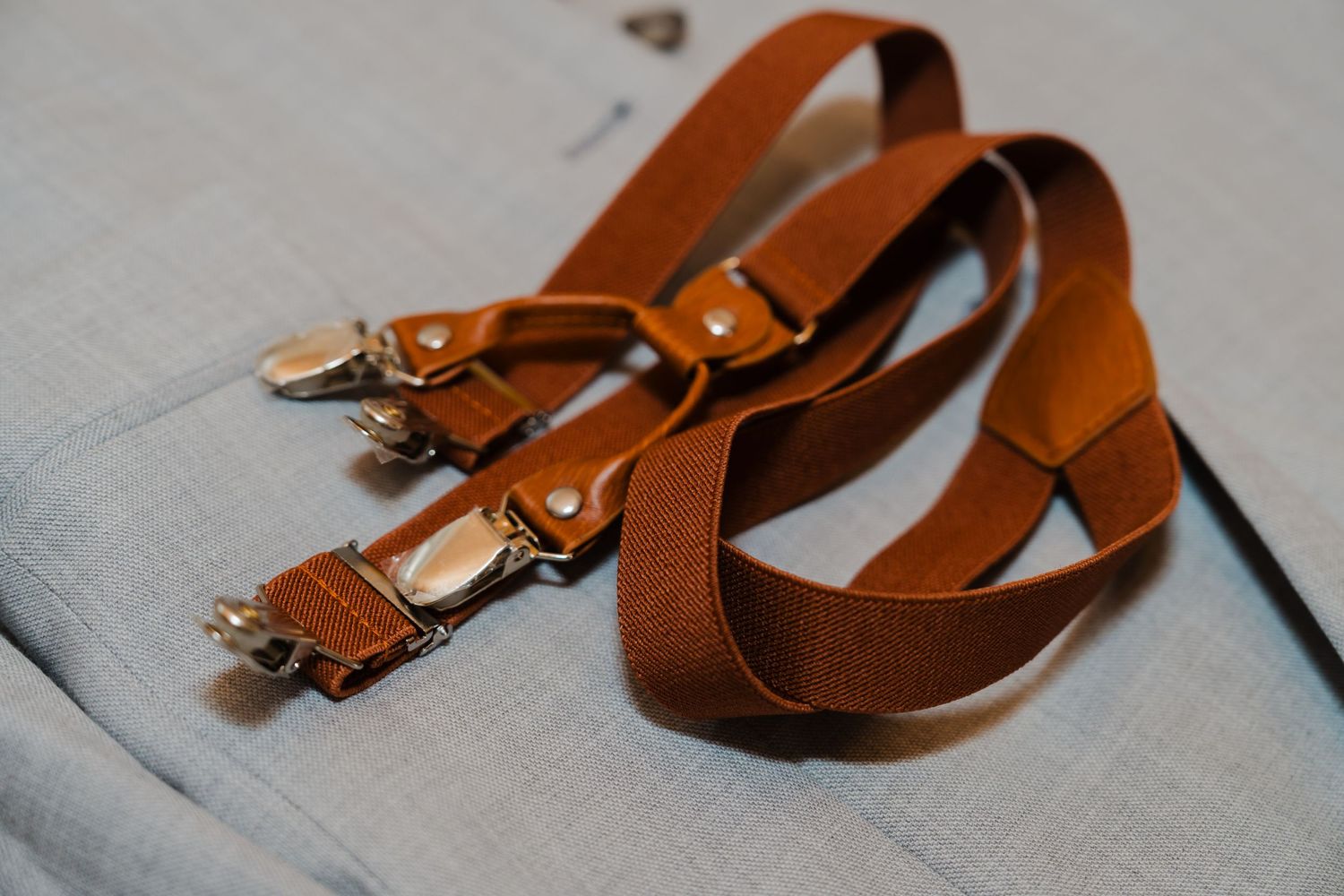 Brown leather suspenders with metal hardware lay flat on a light gray surface.