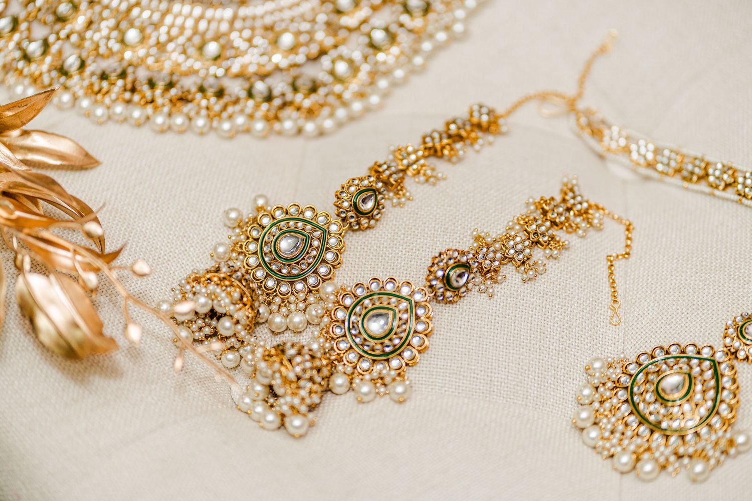 Ornate gold and pearl Indian bridal jewelry set with intricate details on white background.