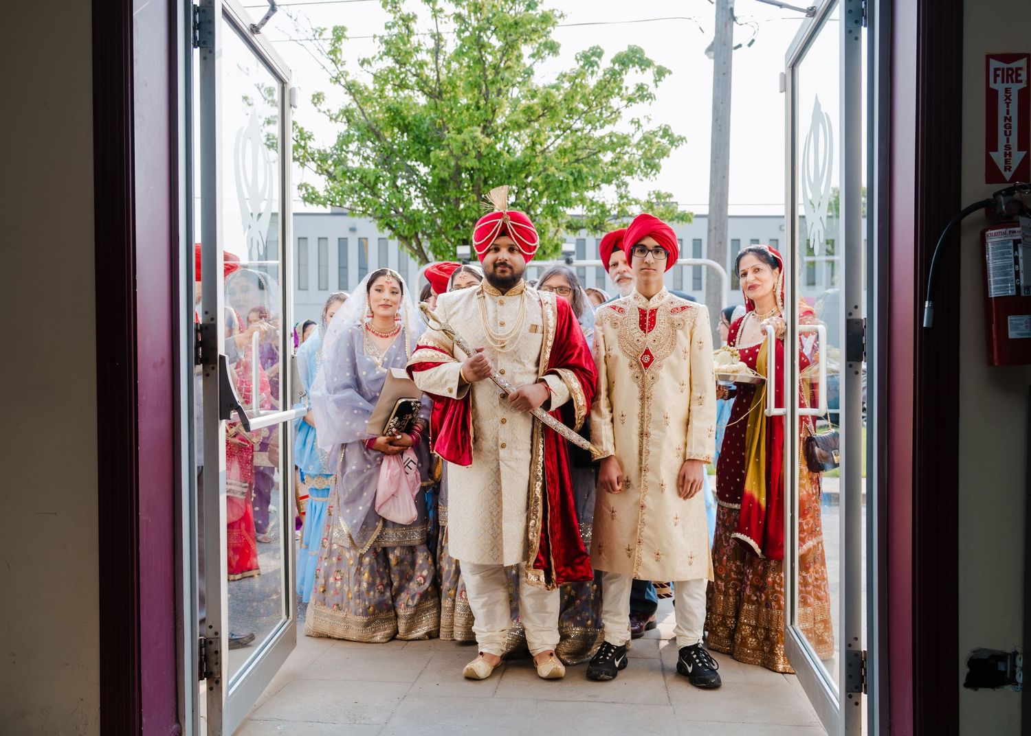 Wedding party members in traditional Indian attire stand together at an entrance doorway.