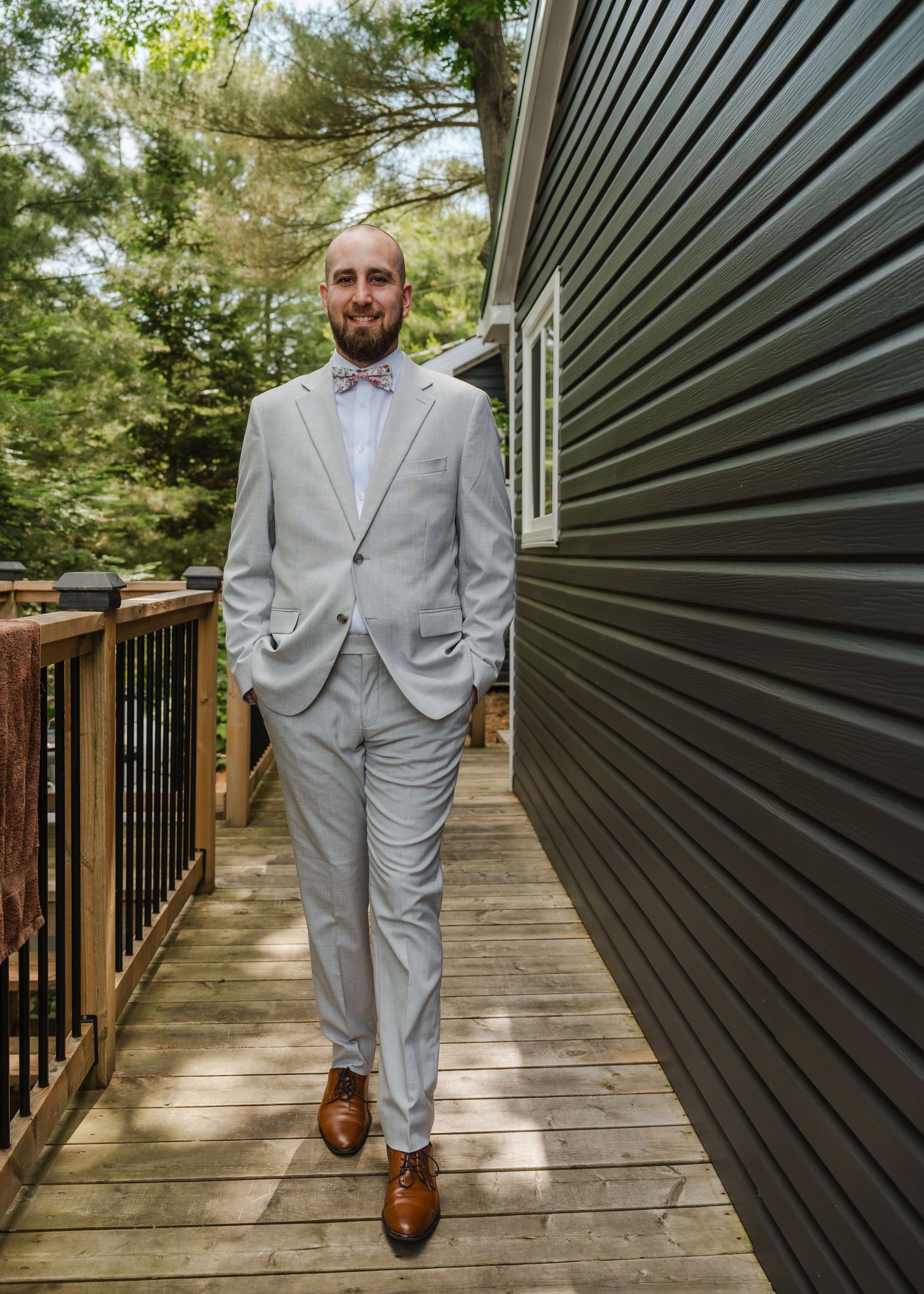 Someone in a light gray suit and brown shoes stands on a wooden deck next to a dark gray building exterior.