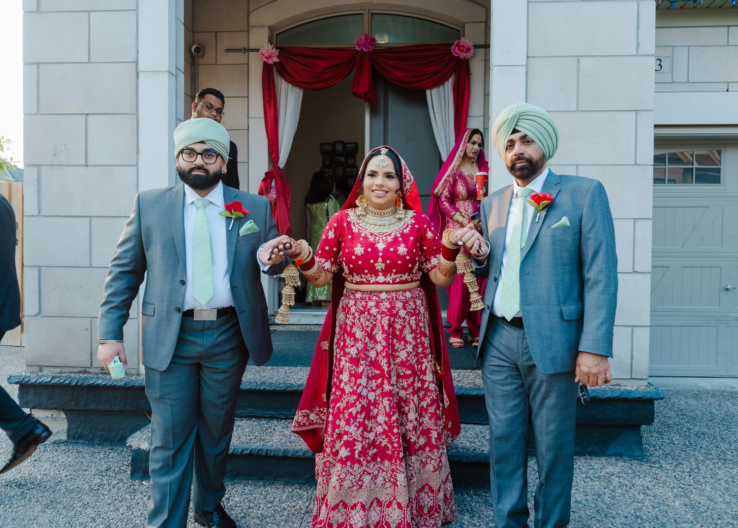 Traditional Indian wedding scene with participants in formal attire gathered under a red canopy entrance.