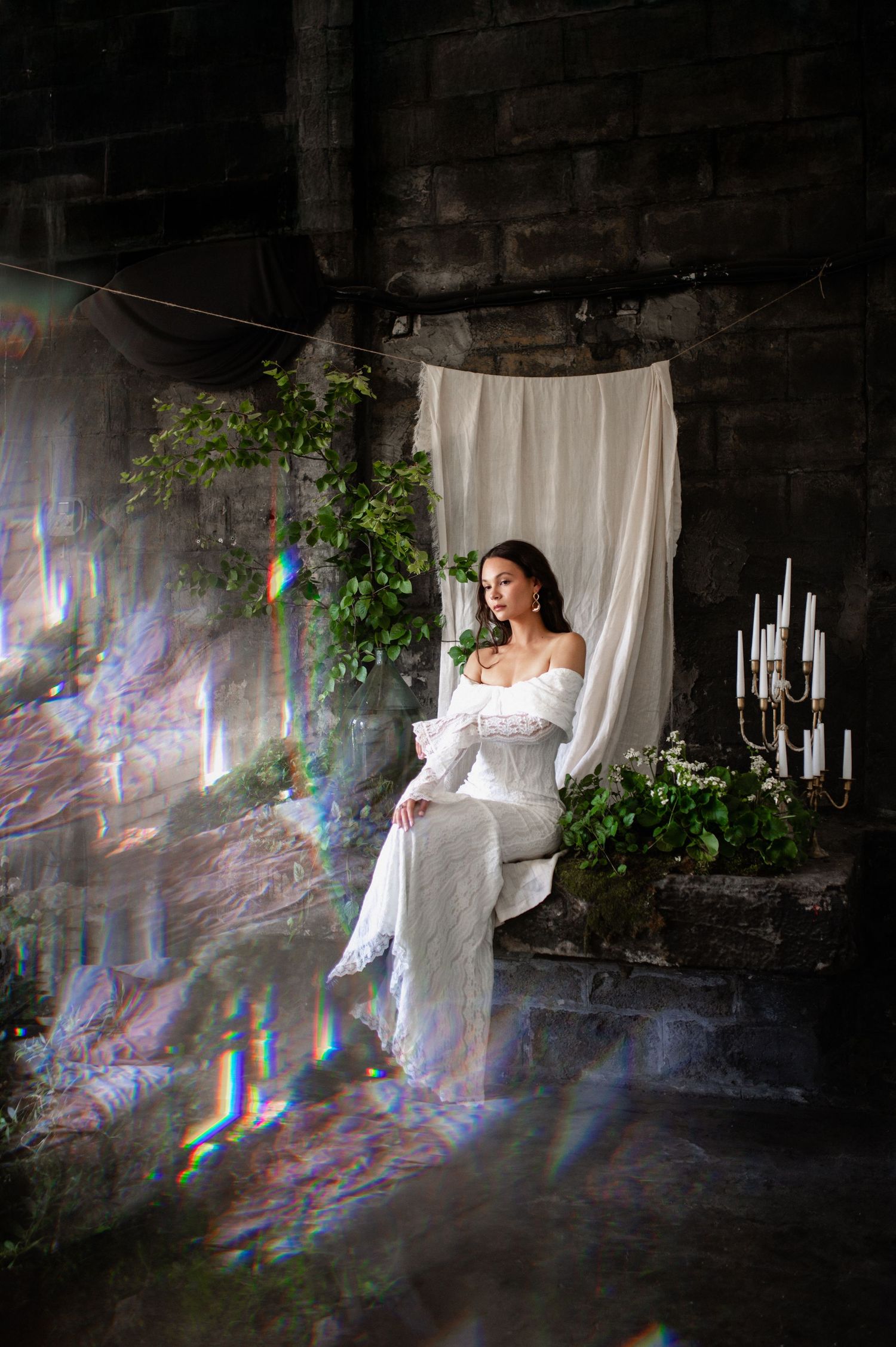Ethereal photoshoot with white fabric and prismatic light effects in a dark stone setting.