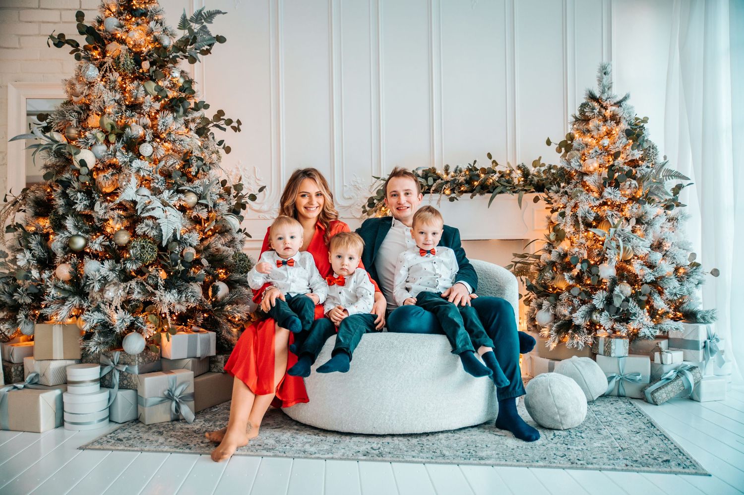 Family lounging together in festive holiday setting with decorated Christmas tree and cozy white furniture.