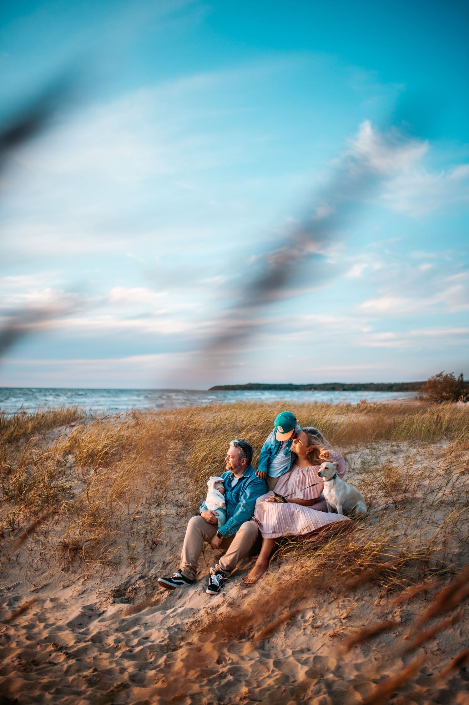 Couple relaxing on sandy beach dunes during sunset with turquoise sky.