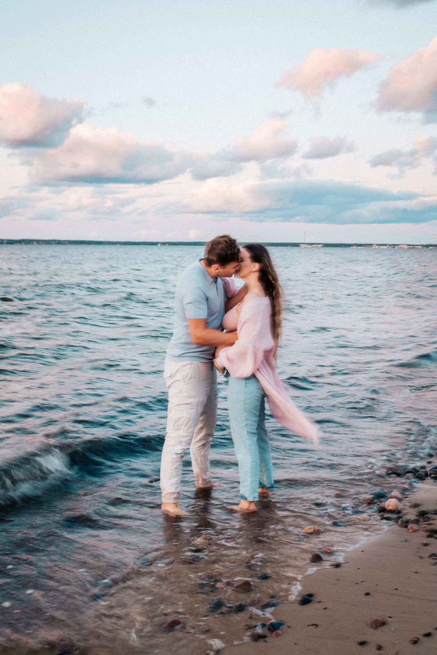 Romantic beach photoshoot at sunset with waves lapping at the shore.