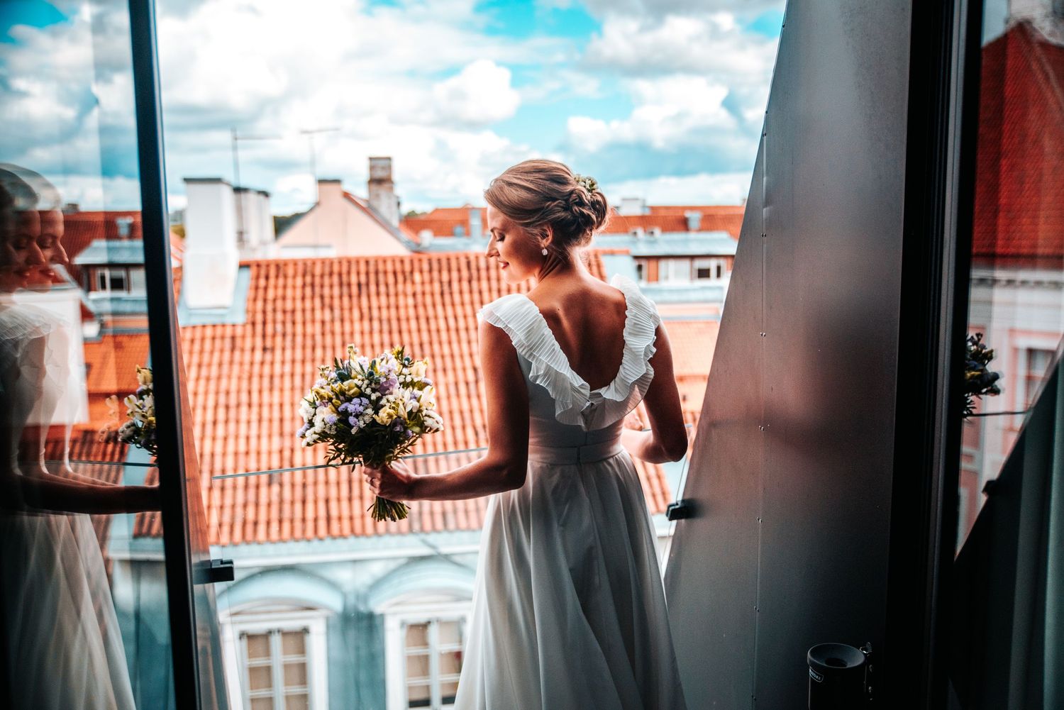 Sunlit bridal preparation scene through windows with city rooftops in background.