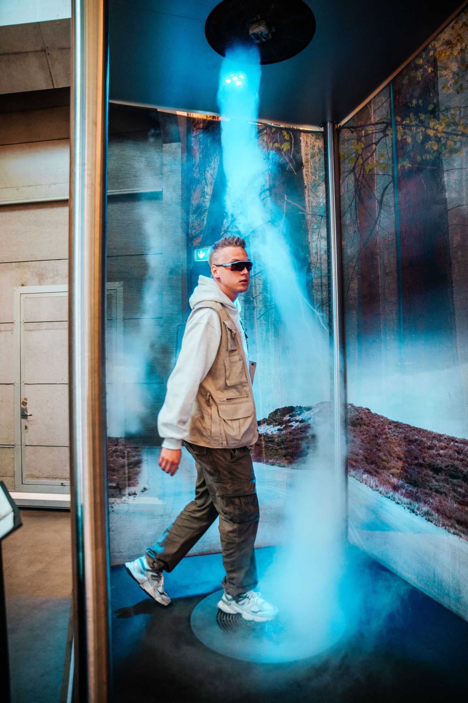 Person in utility vest walks through dramatic blue smoke effects in an industrial hallway setting.