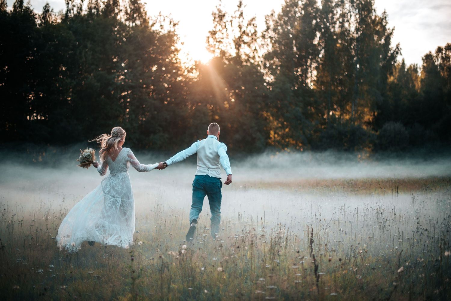 Dreamy wedding photos in misty field during sunset with flowing dress.