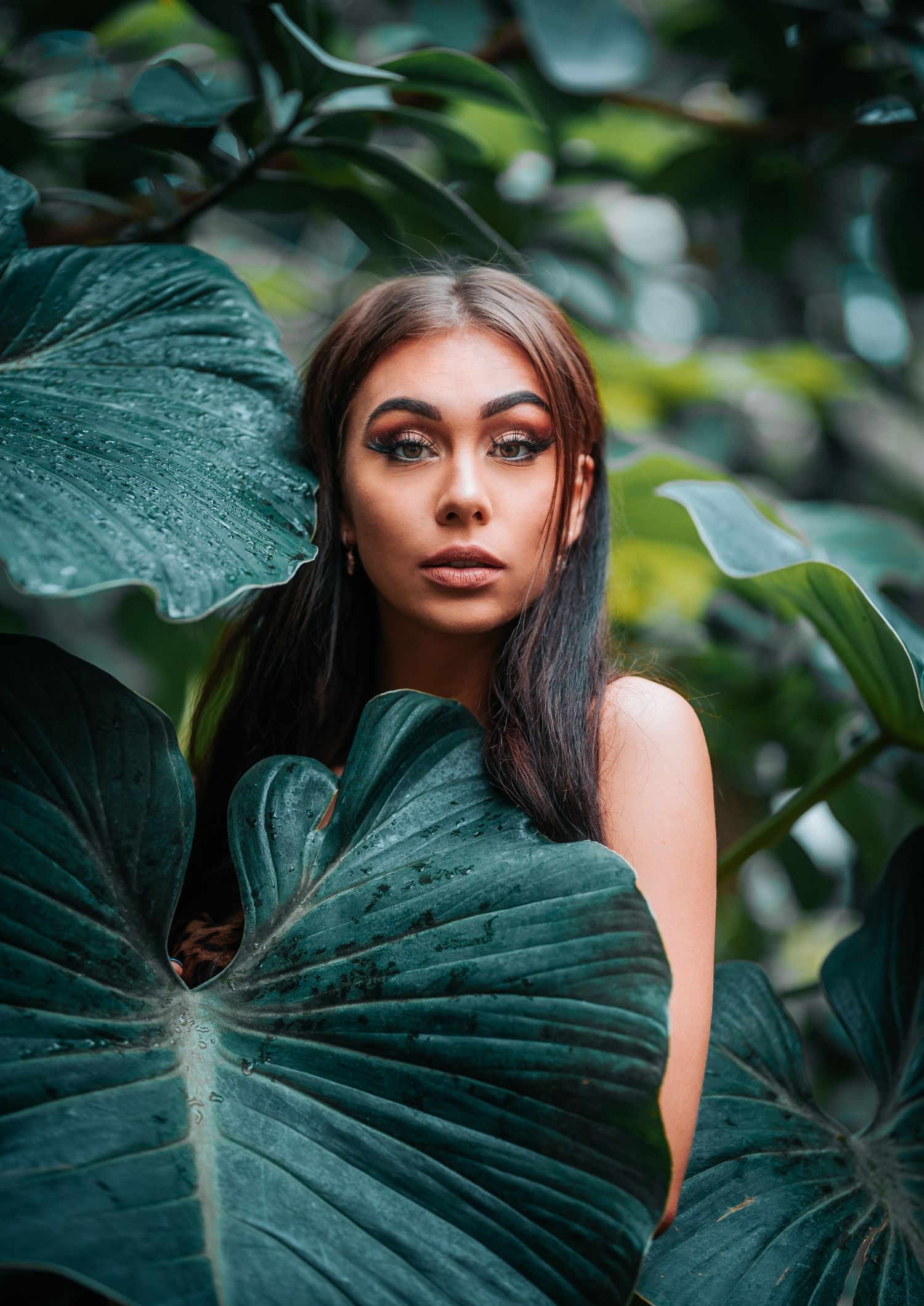 Creative fashion portrait framed by large green monstera leaves in moody lighting.