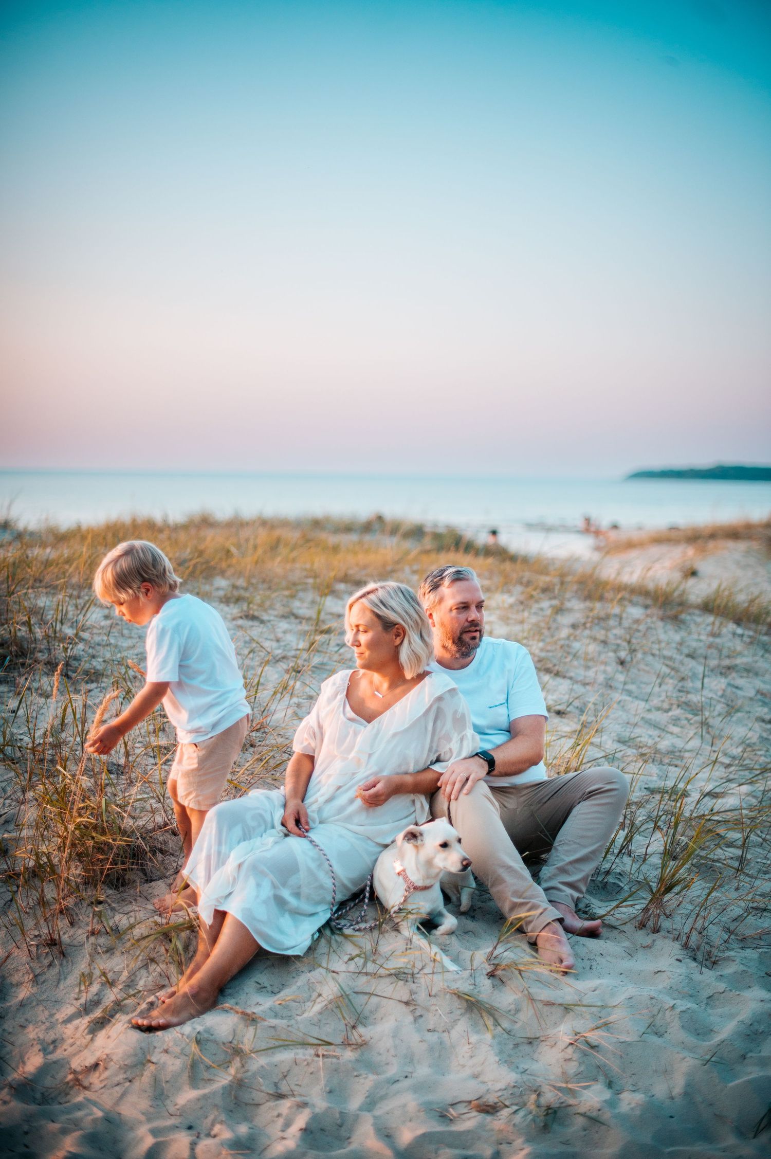 Playful beach photoshoot at sunset with casual attire and natural sand dune backdrop.
