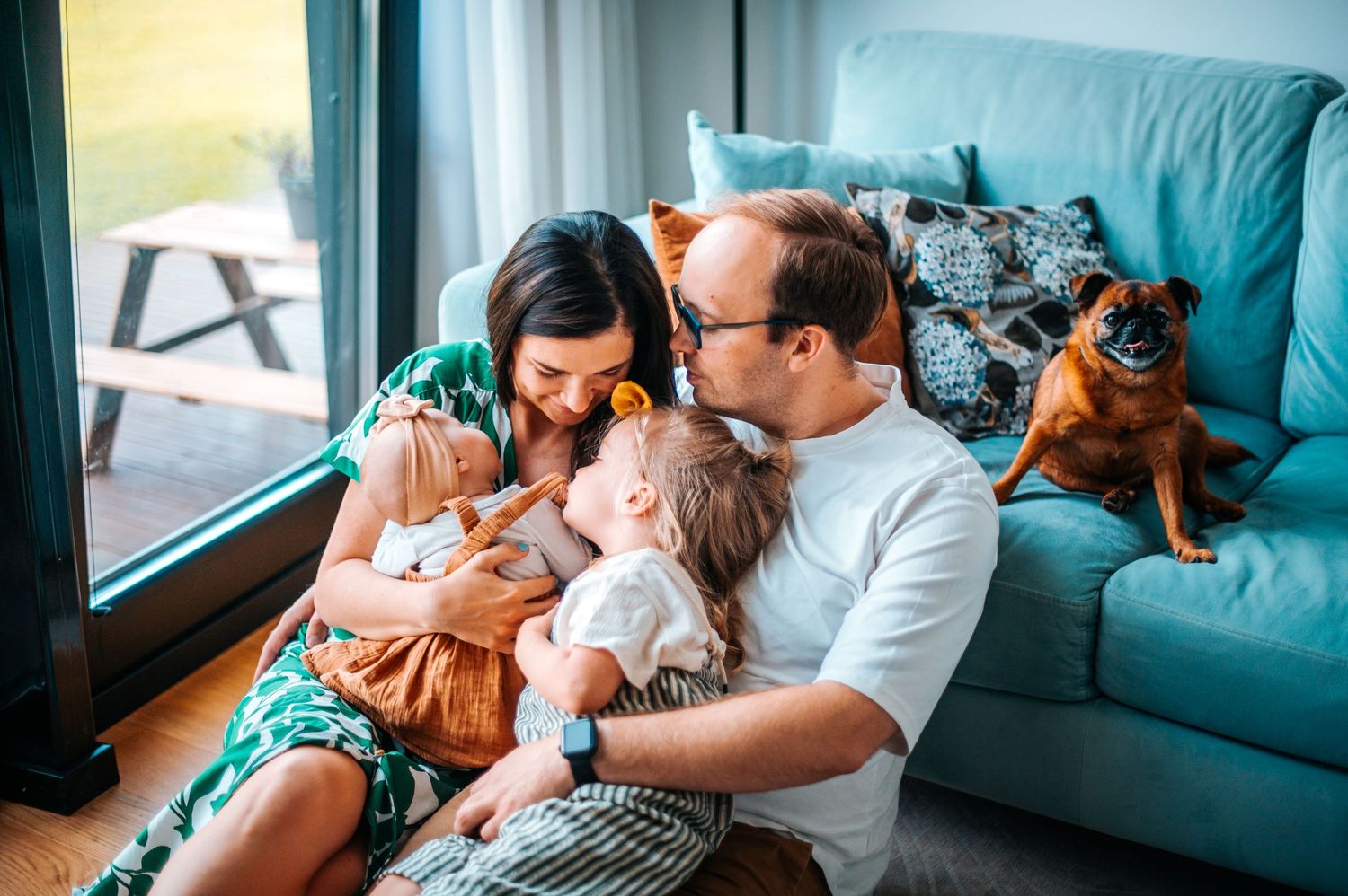 Couple relaxing on teal couch with cat sharing intimate moment in bright living room.