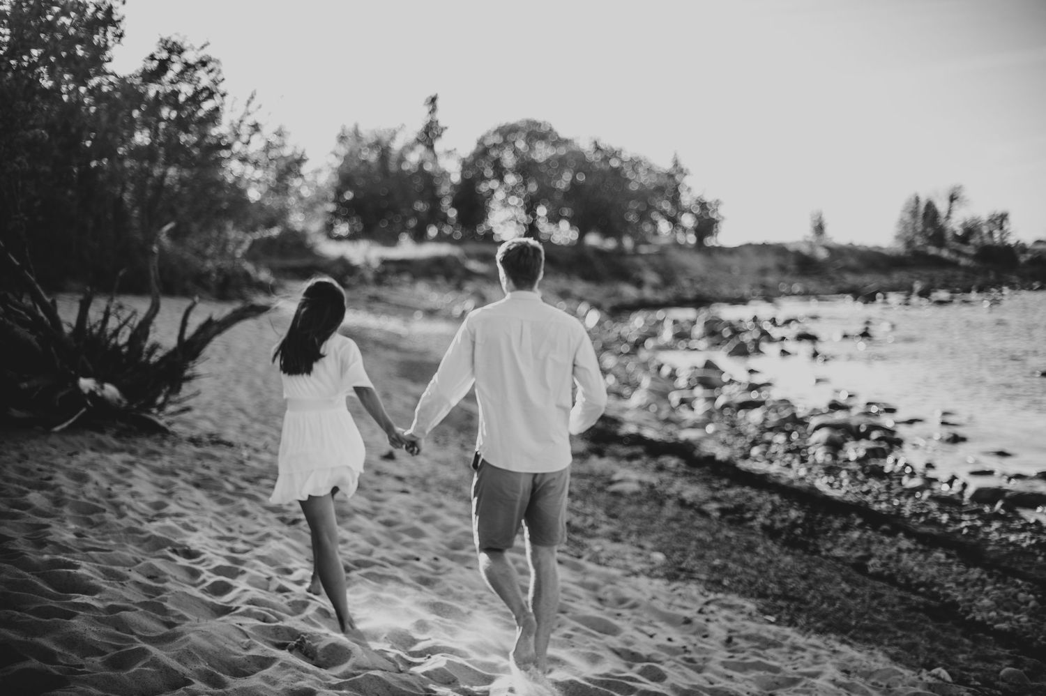 Black and white photo of couple walking along rocky beach shoreline.