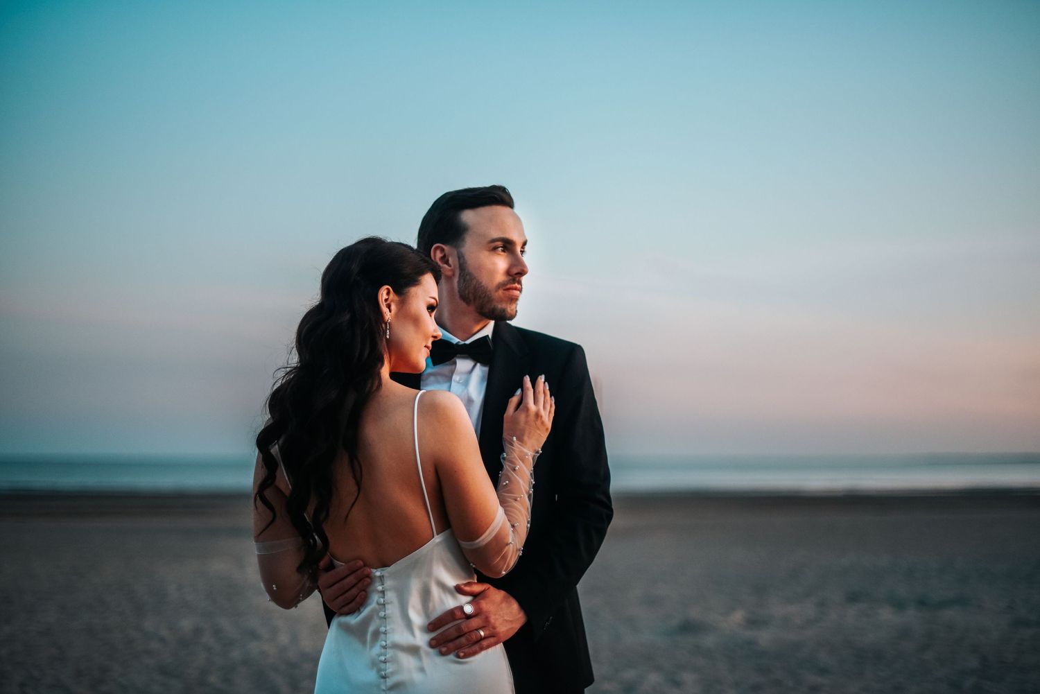 A romantic sunset wedding portrait captured against a soft blue sky.
