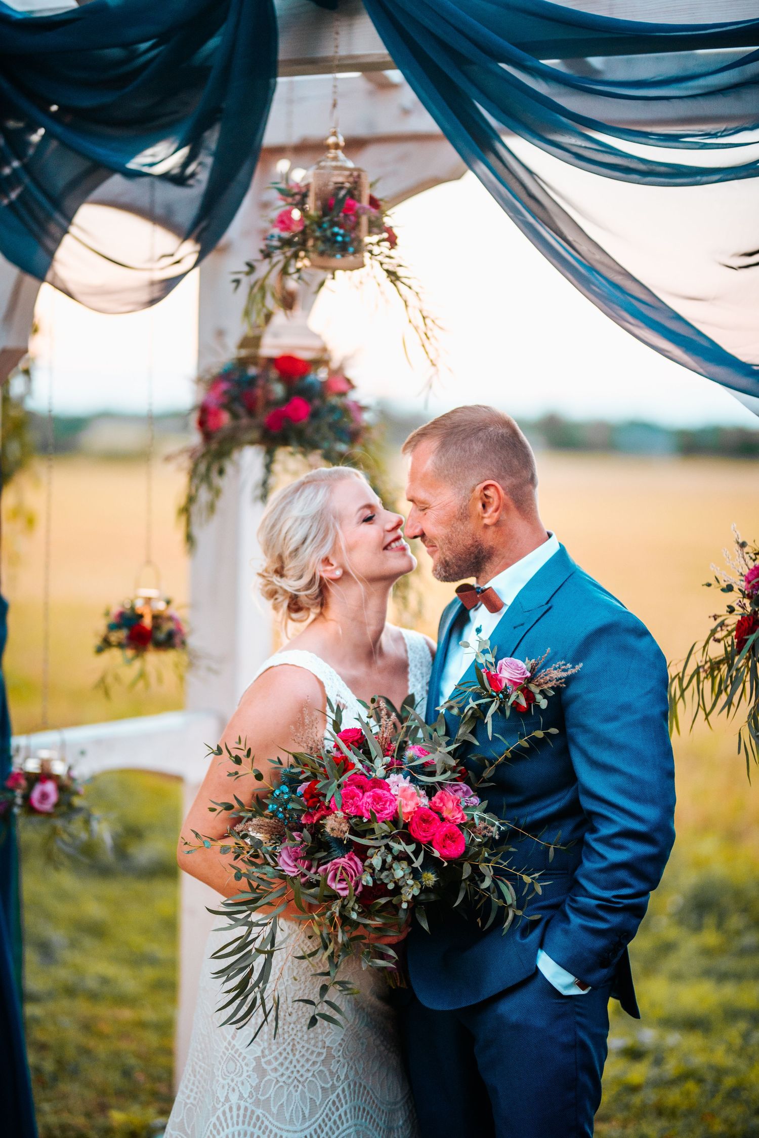 Romantic wedding ceremony under draped navy blue fabric with vibrant floral arrangements.