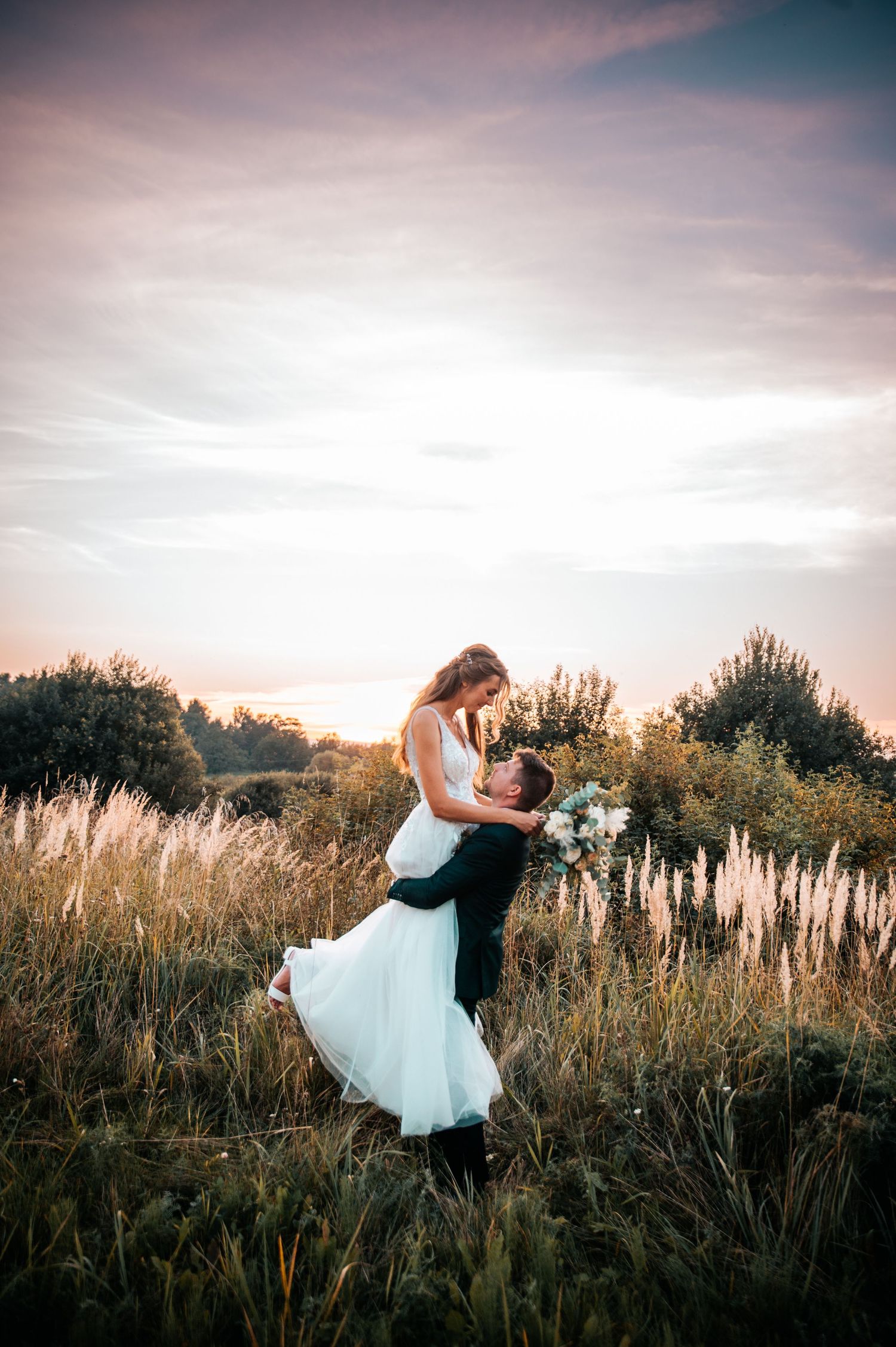 Romantic sunset wedding photo of couple embracing in field of tall grass.