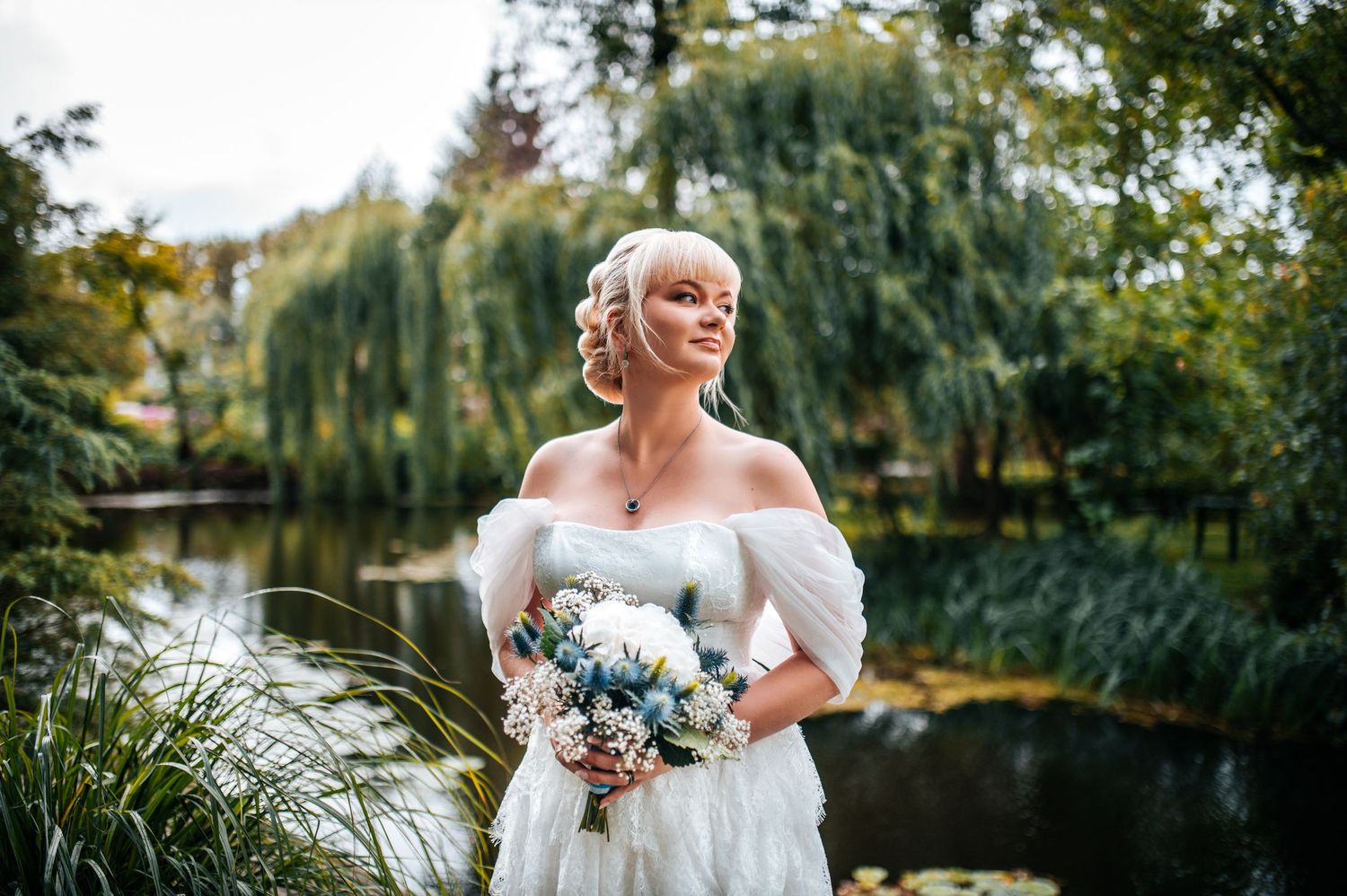 A bride in a white dress stands in a garden setting surrounded by lush greenery.
