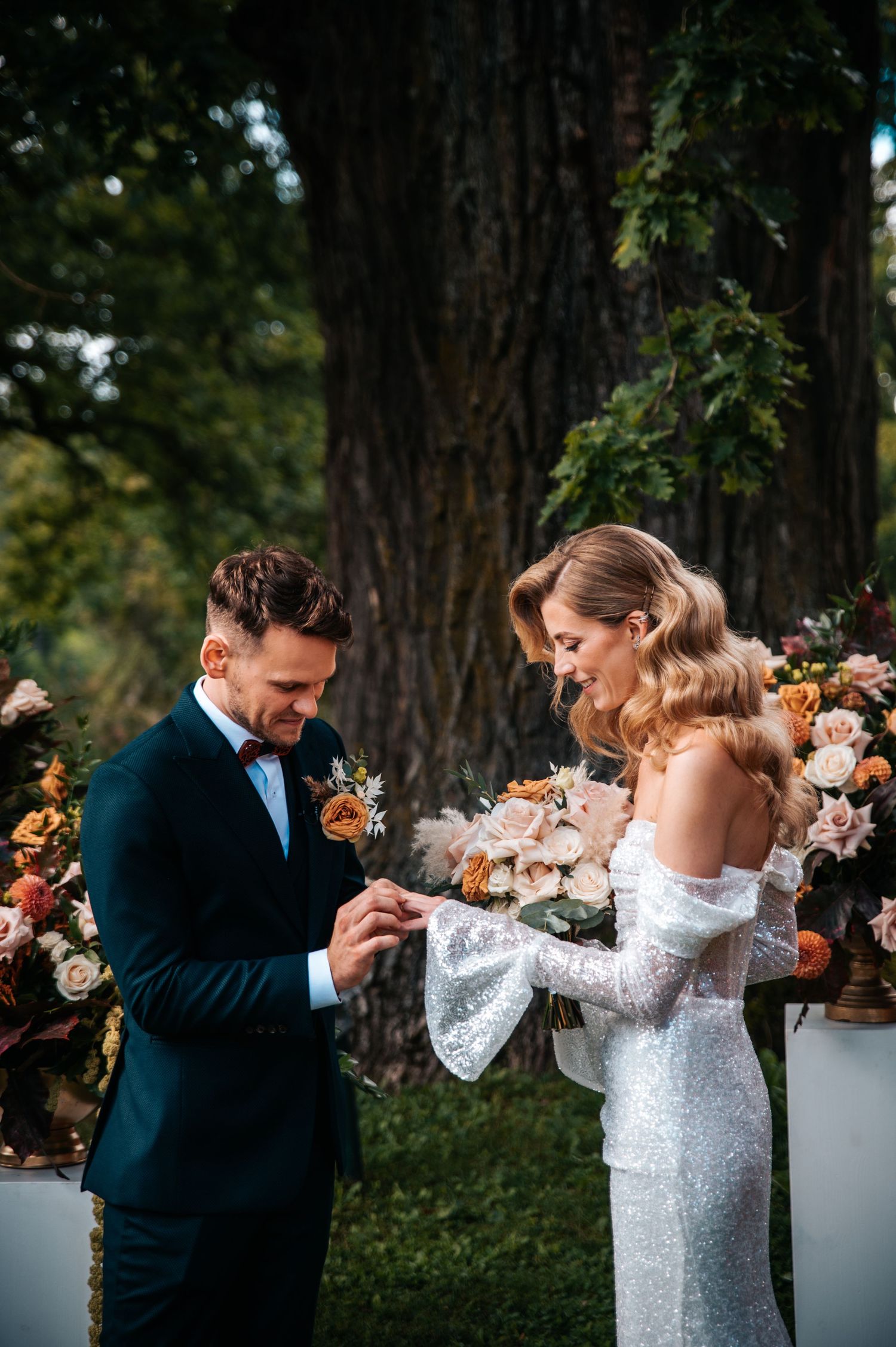 Couple in formal attire dancing outdoors surrounded by autumn trees.